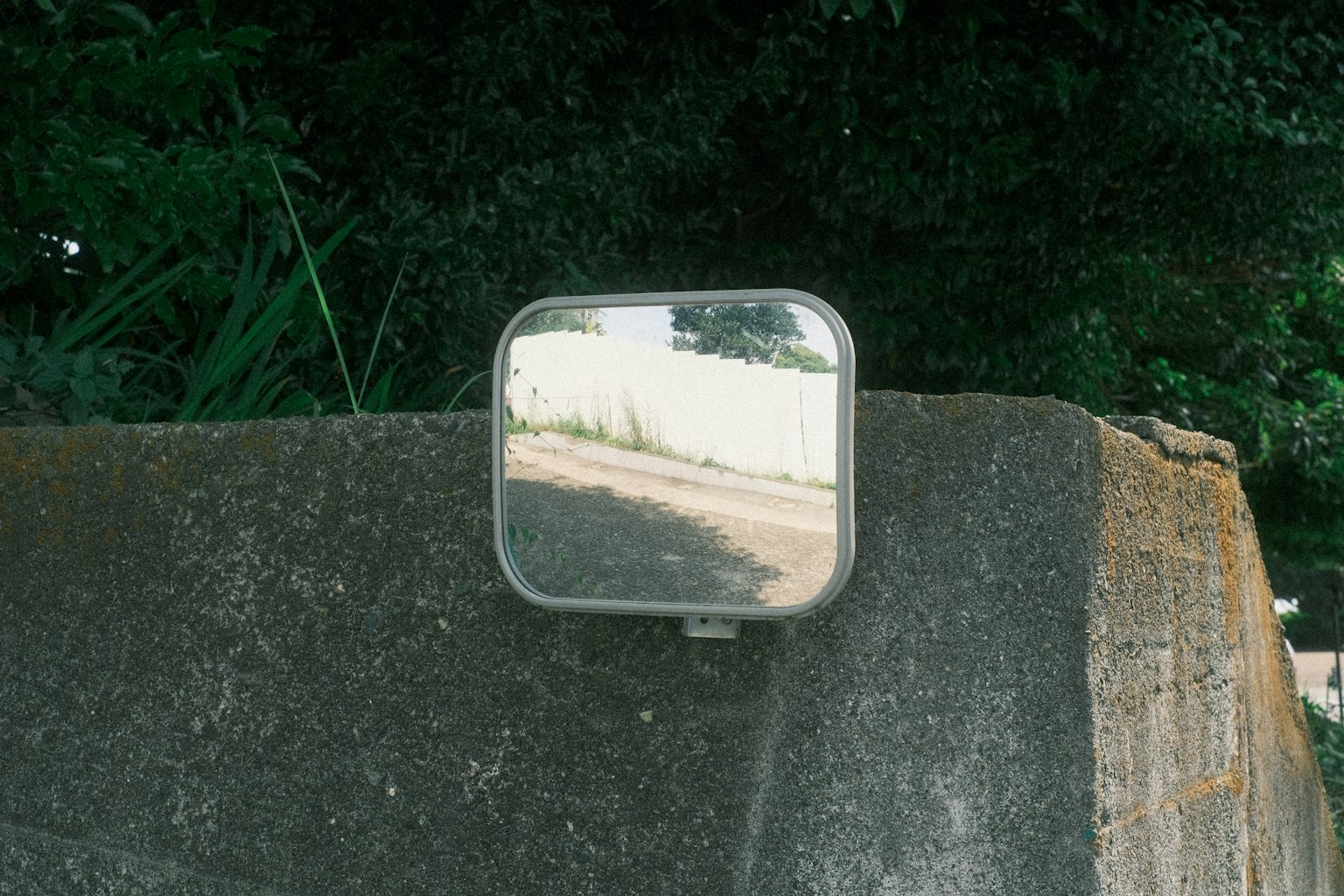Specchio quadrato che riflette una strada montato su un muro di cemento