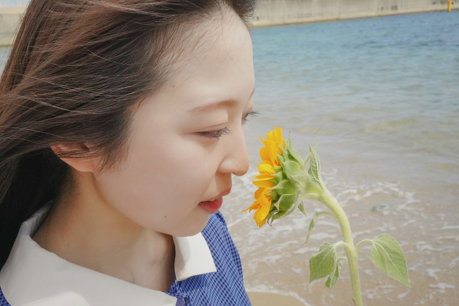 Perfil de una mujer sosteniendo un girasol junto al mar