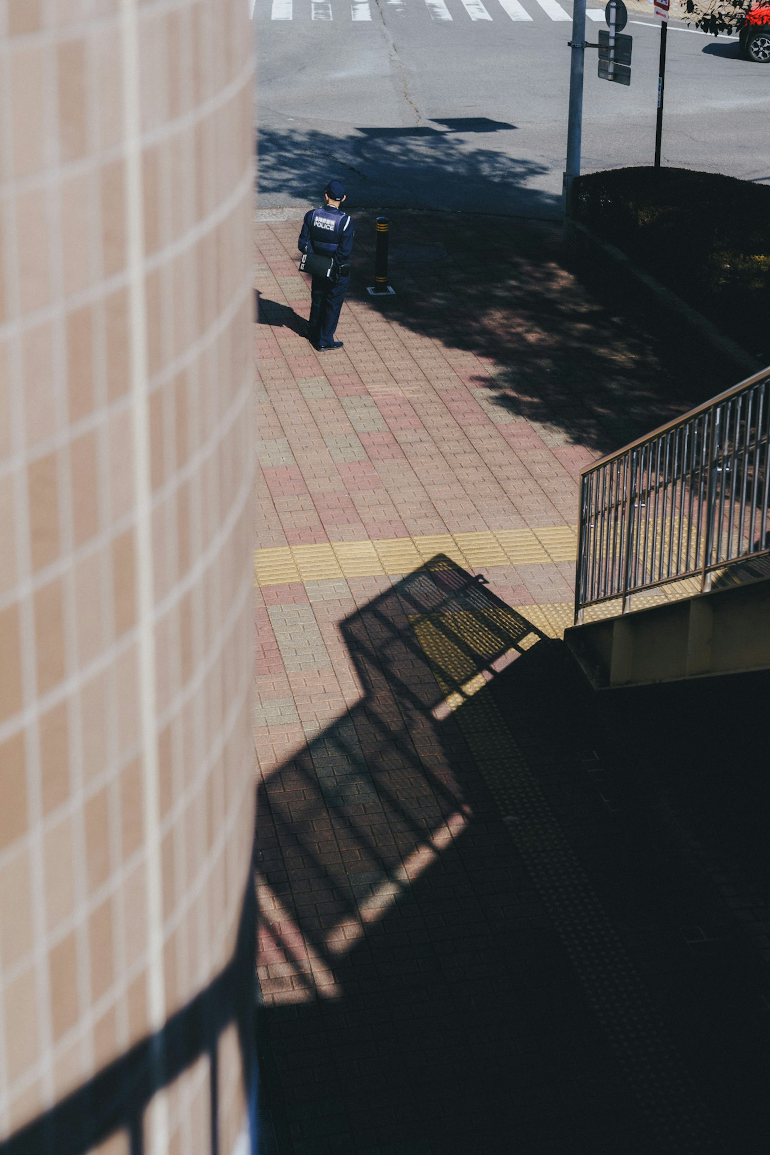 Un oficial de policía caminando por la acera con sombras y patrones de edificio visibles