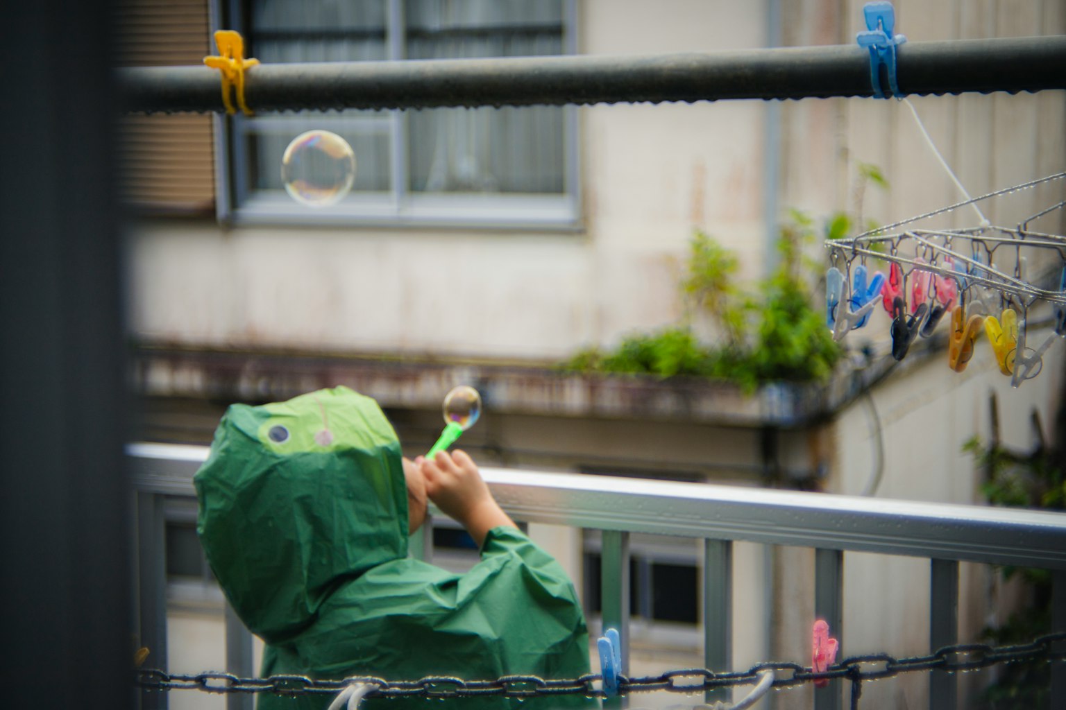 一个穿着绿色雨衣的孩子在户外吹泡泡