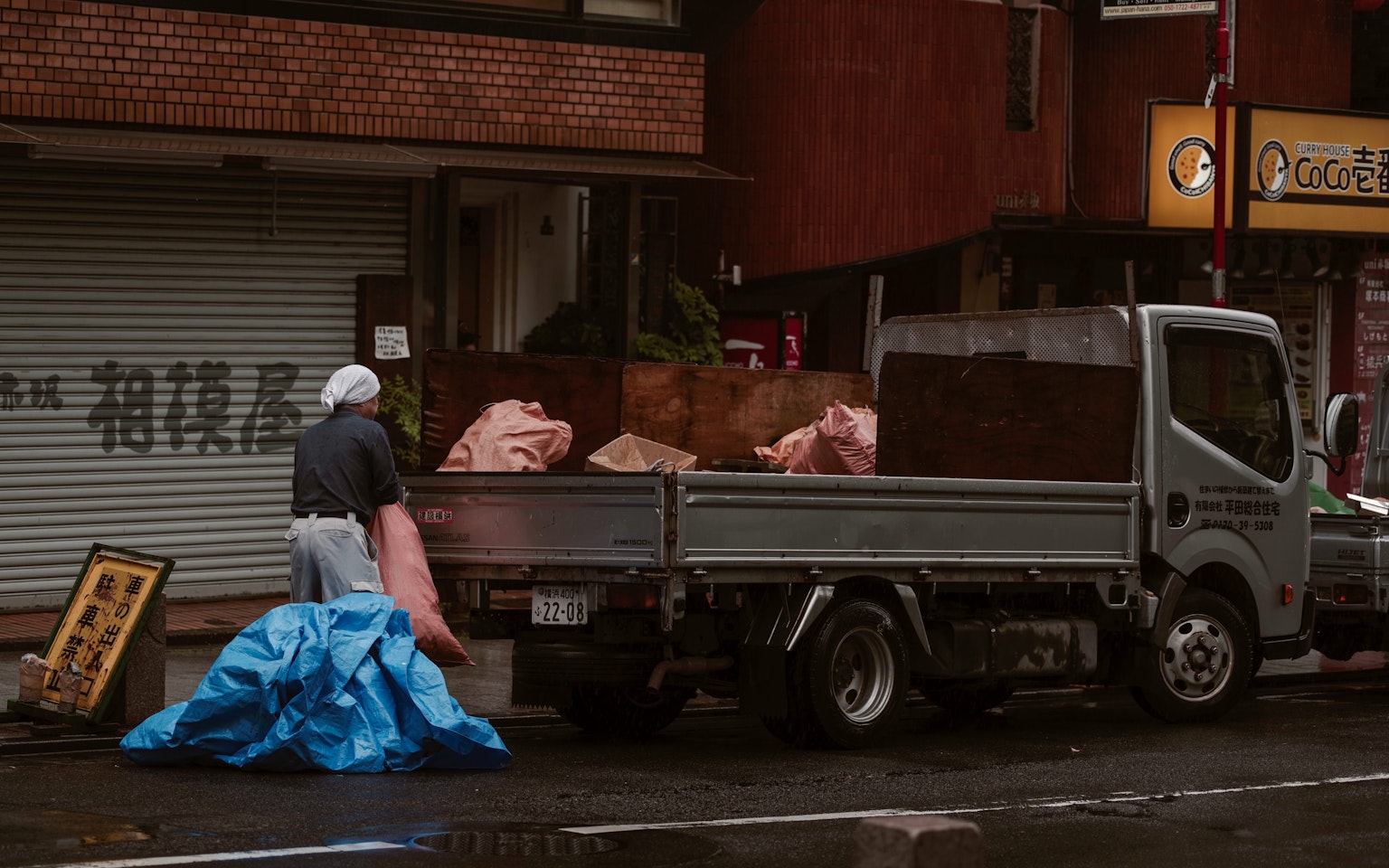 Worker loading items onto a truck with a blue tarp in an urban setting