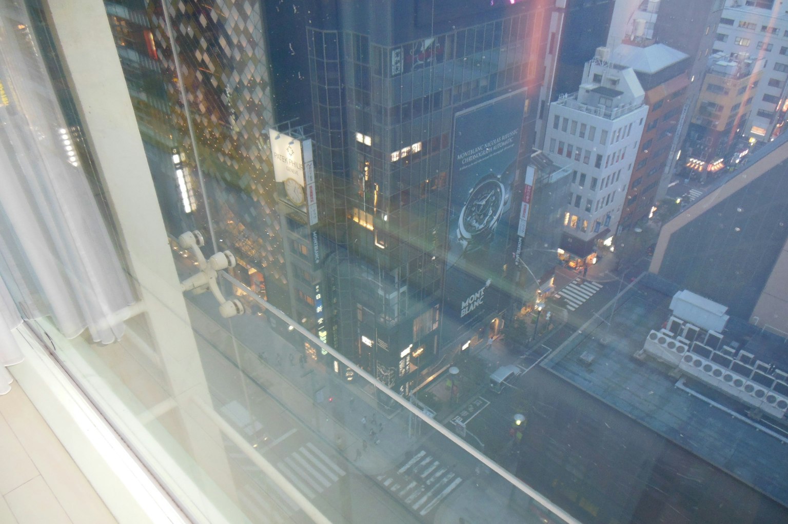Vista notturna di una città dalla finestra di un grattacielo con luci stradali e riflessi degli edifici