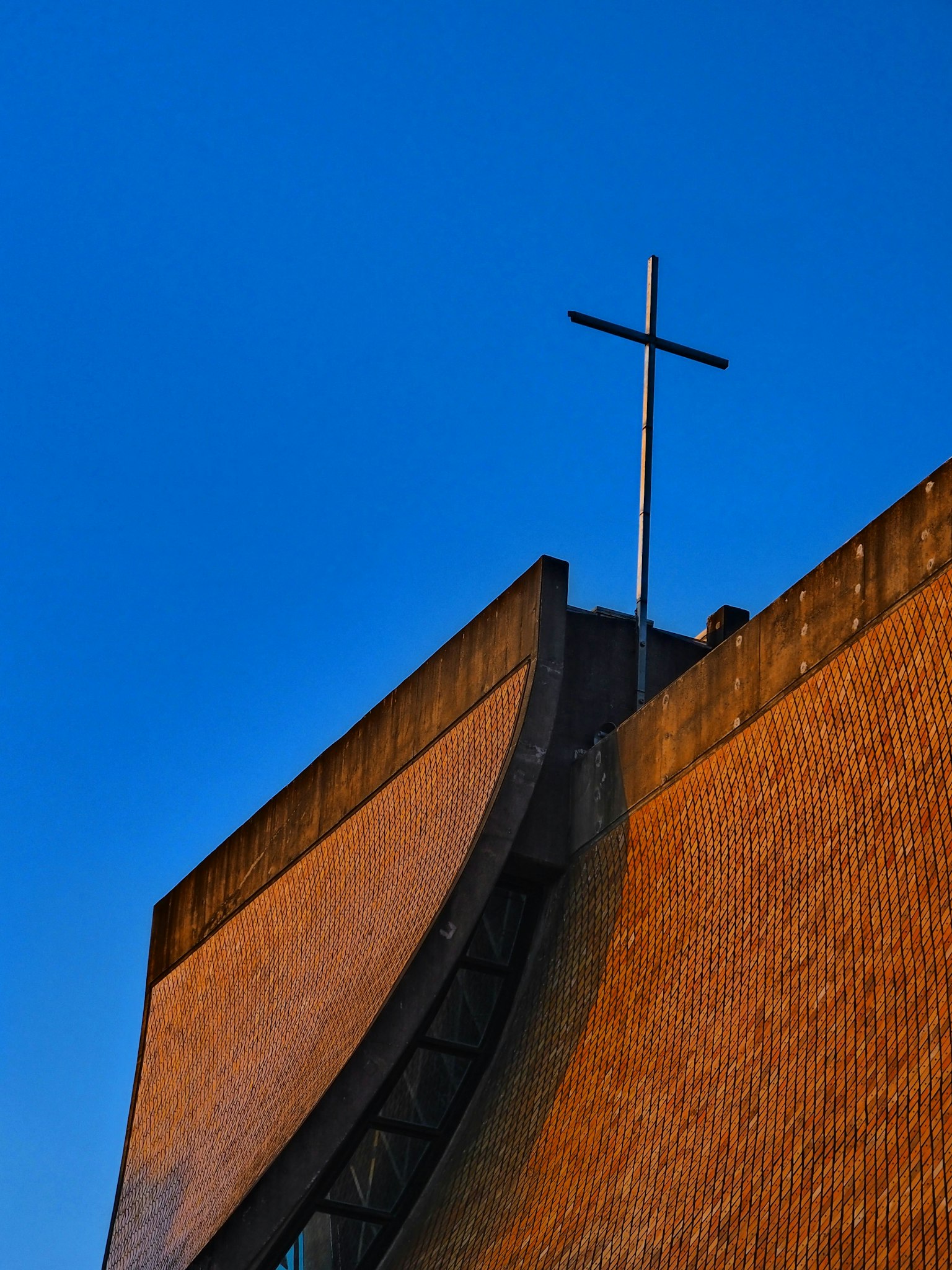 Part of a church roof with a cross under a blue sky