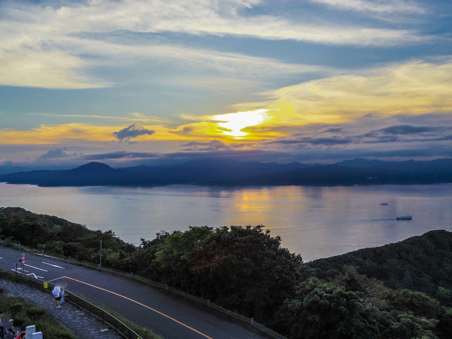 ทิวทัศน์ที่สวยงามของพระอาทิตย์ตกเหนือทะเลกับเนินเขาสีเขียว