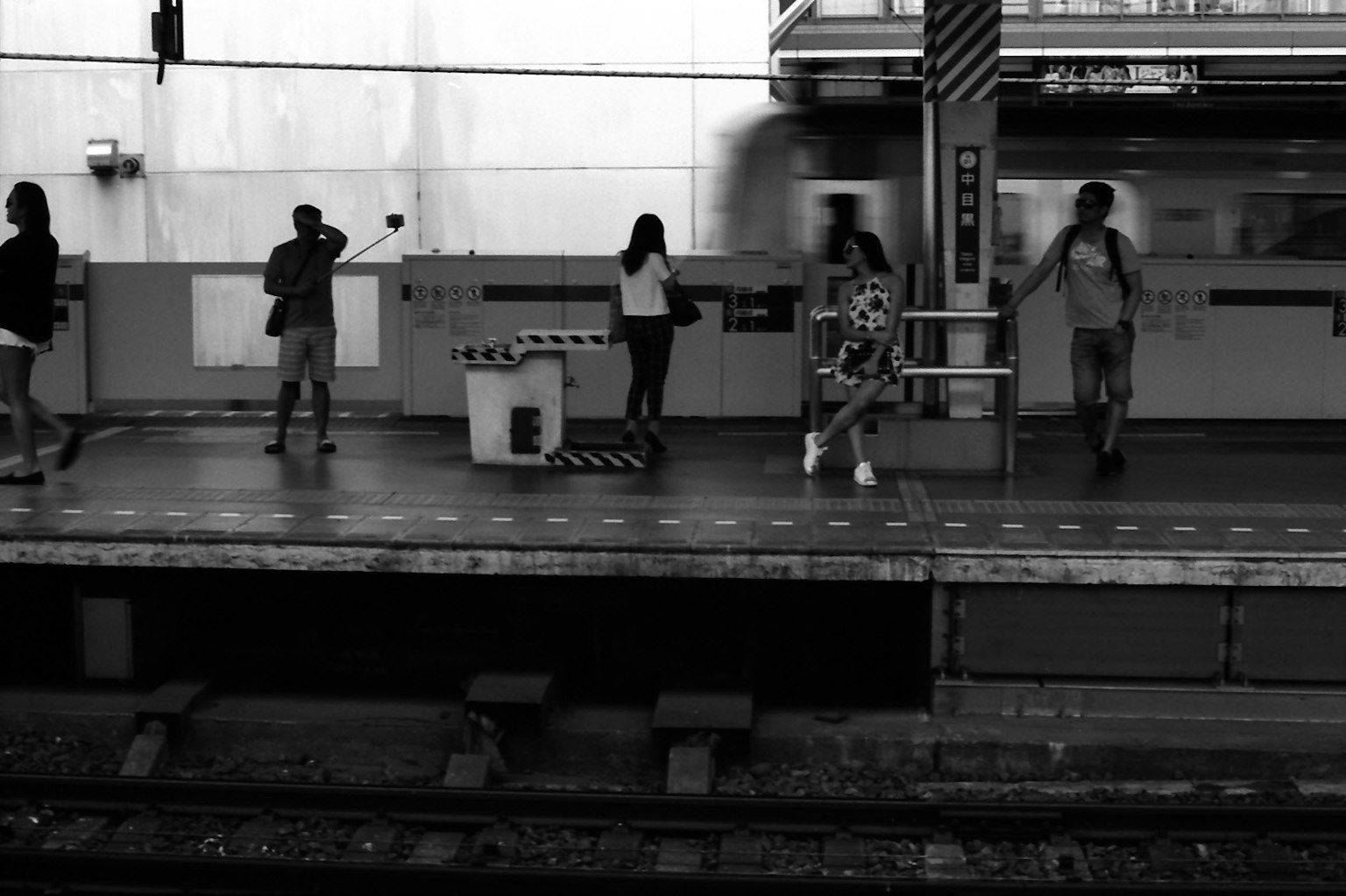 Black and white image of passengers standing on a train platform with a passing train