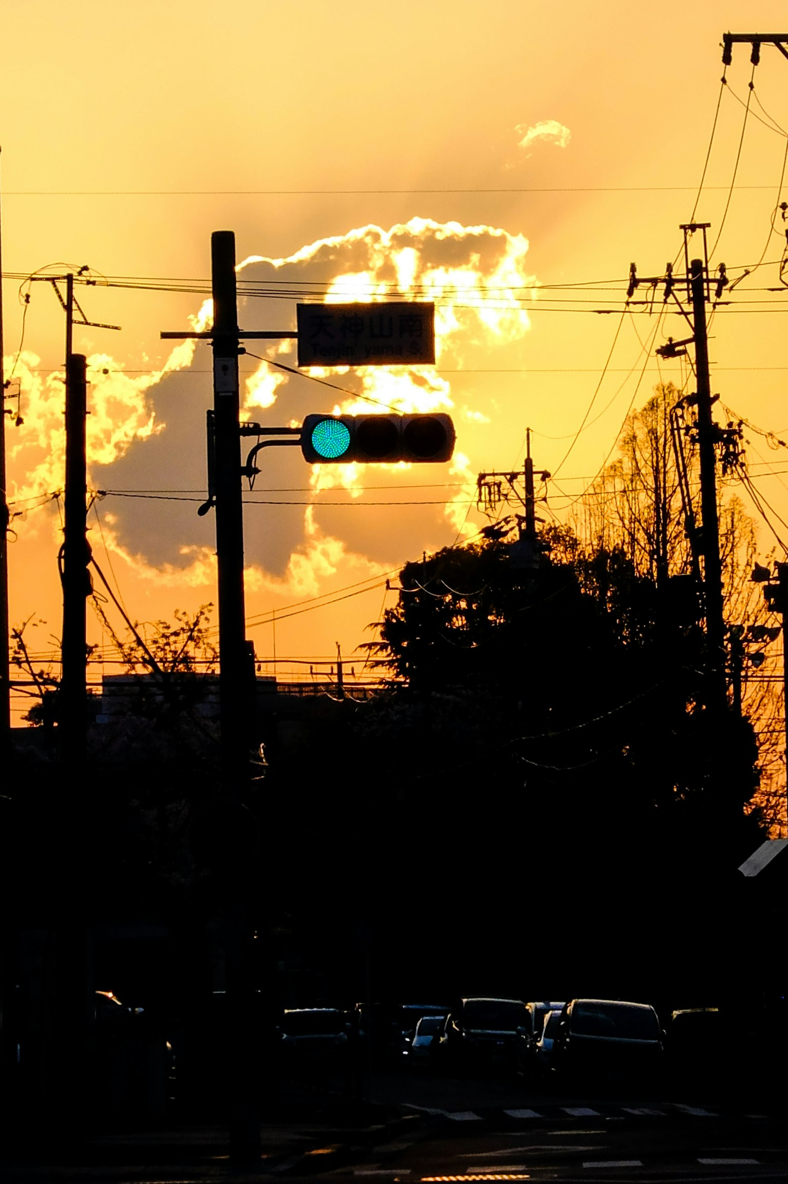 Silhouette of traffic light and utility poles against a sunset sky