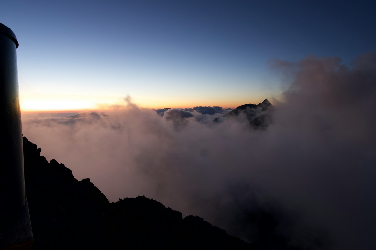 Silhouette of mountains emerging from clouds against a bright sky