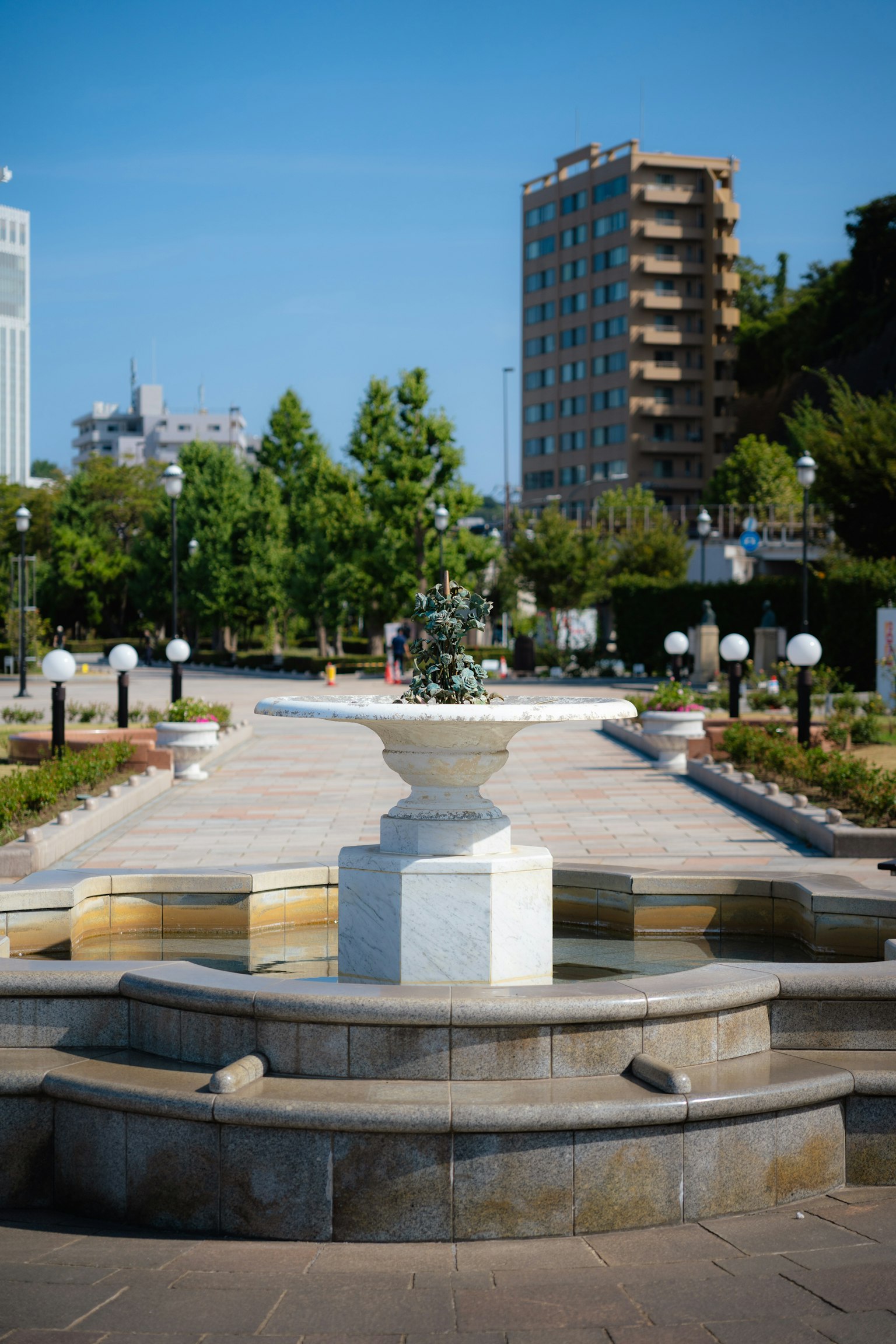 Fontana bianca al centro di un parco circondata da alberi verdi