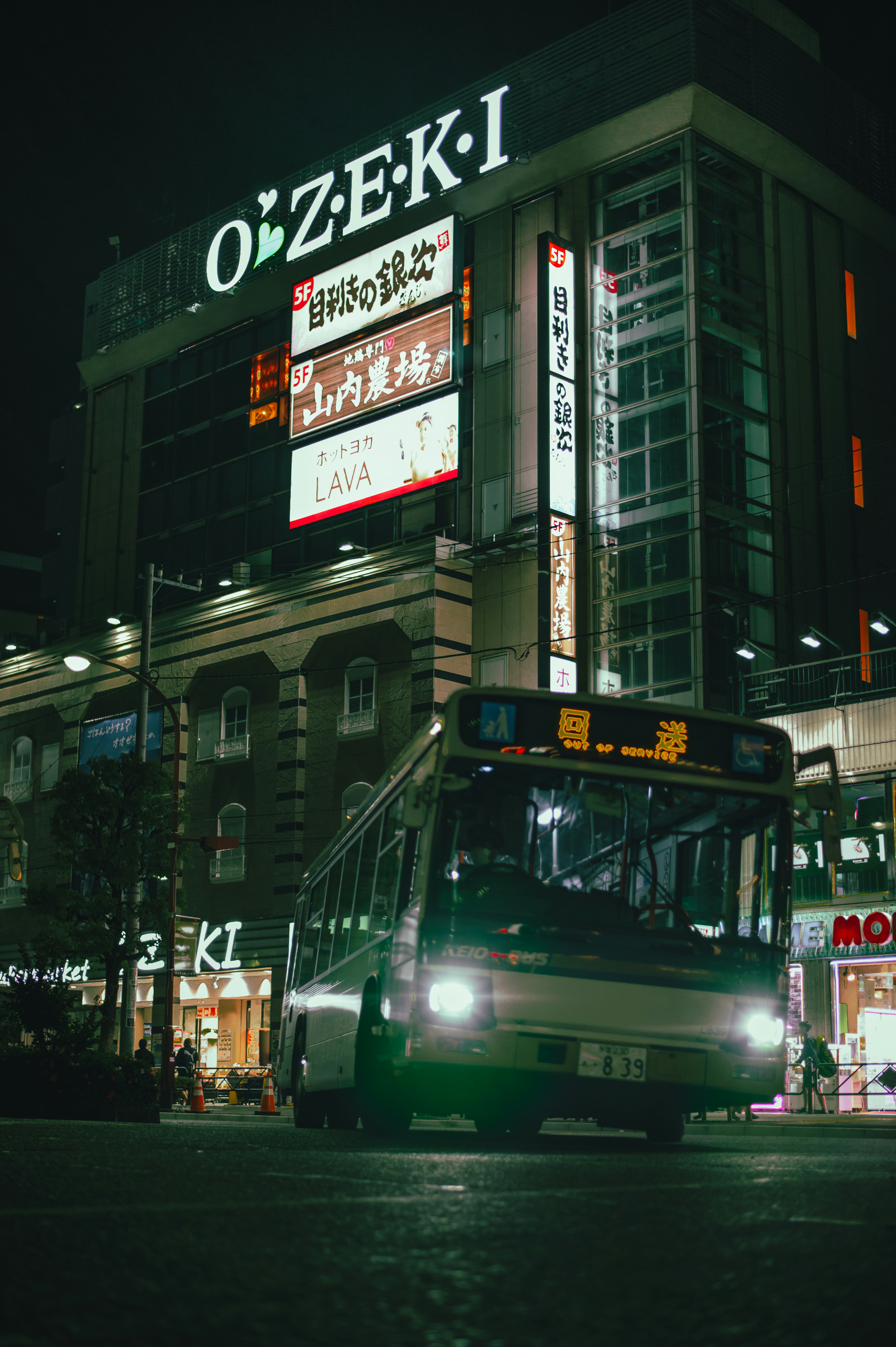 夜の街角で停車するバスと看板のある商業施設の外観