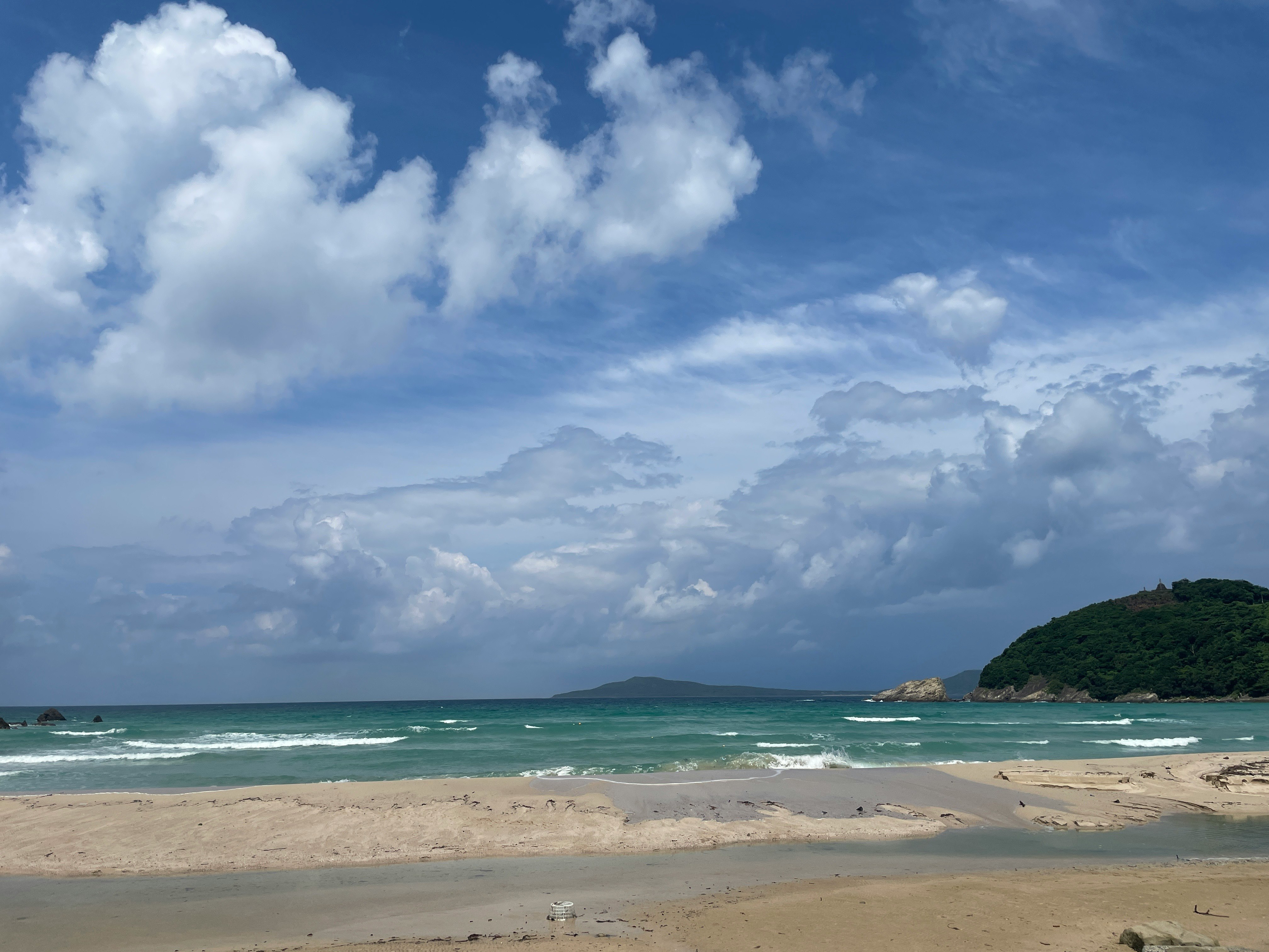 初夏のエメラルドの海と白い波、青い空の下の砂浜