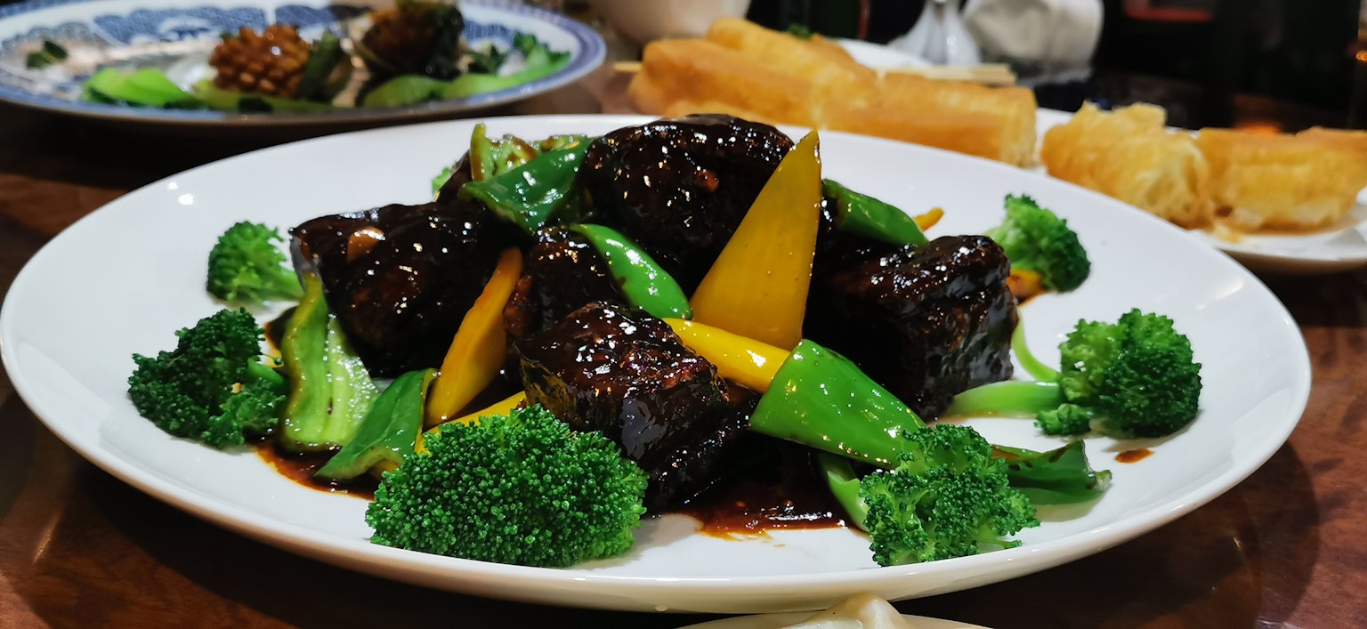 Dish featuring broccoli and snap peas in a black sauce with yellow bell peppers