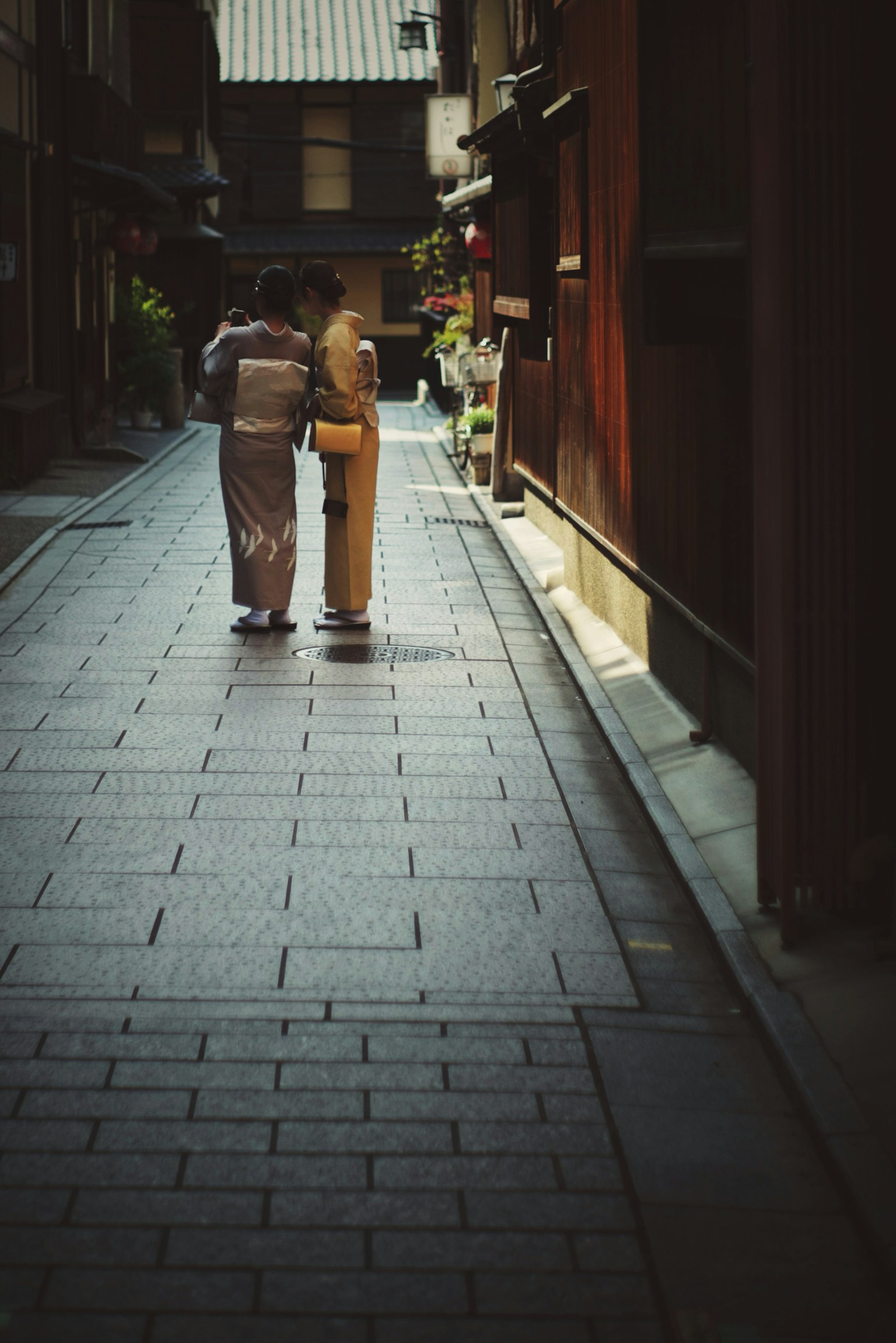 伝統的な着物を着た二人の女性が狭い路地で会話している風景