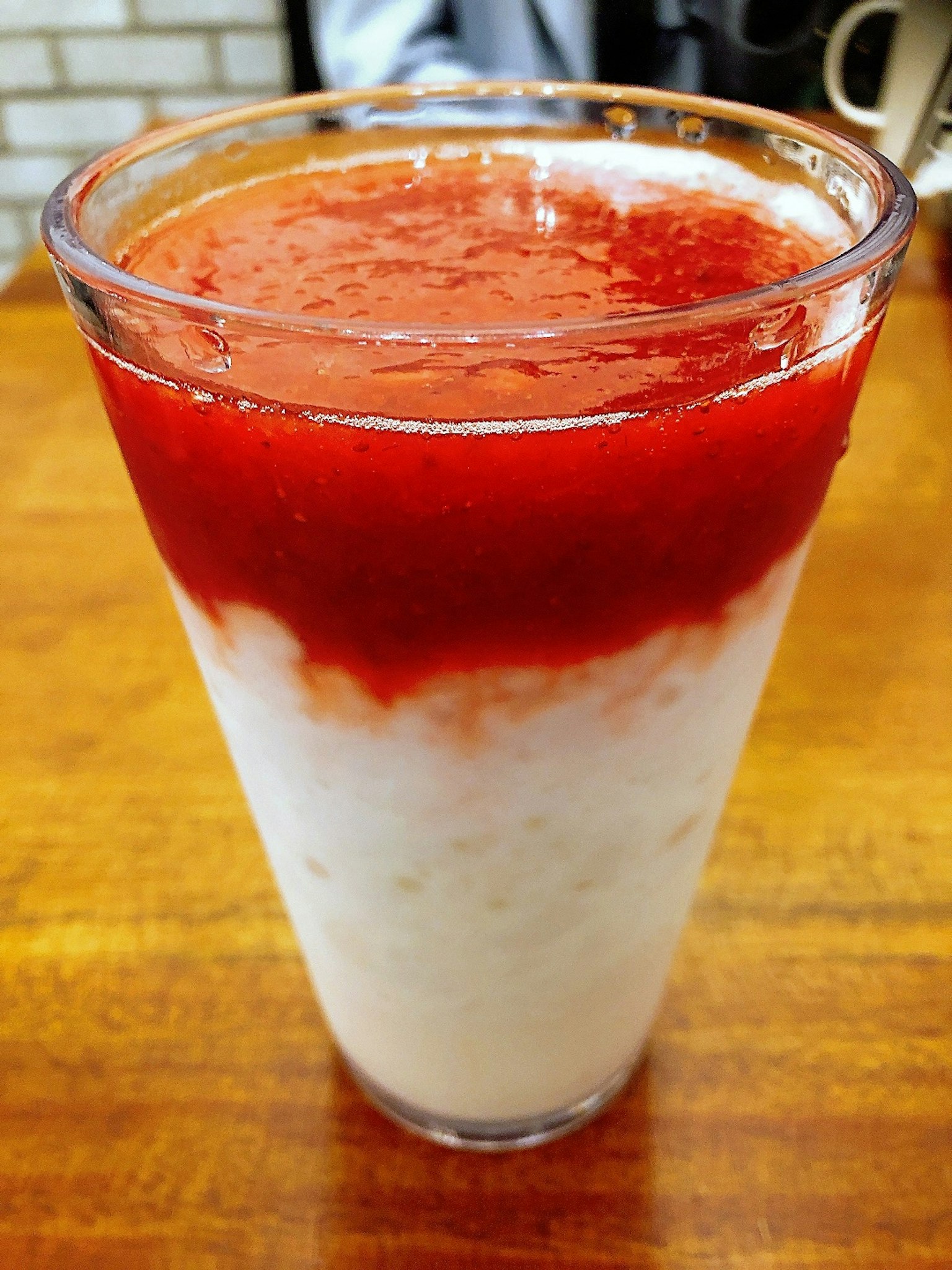 Un verre transparent rempli d'une boisson blanche surmontée d'une sauce rouge