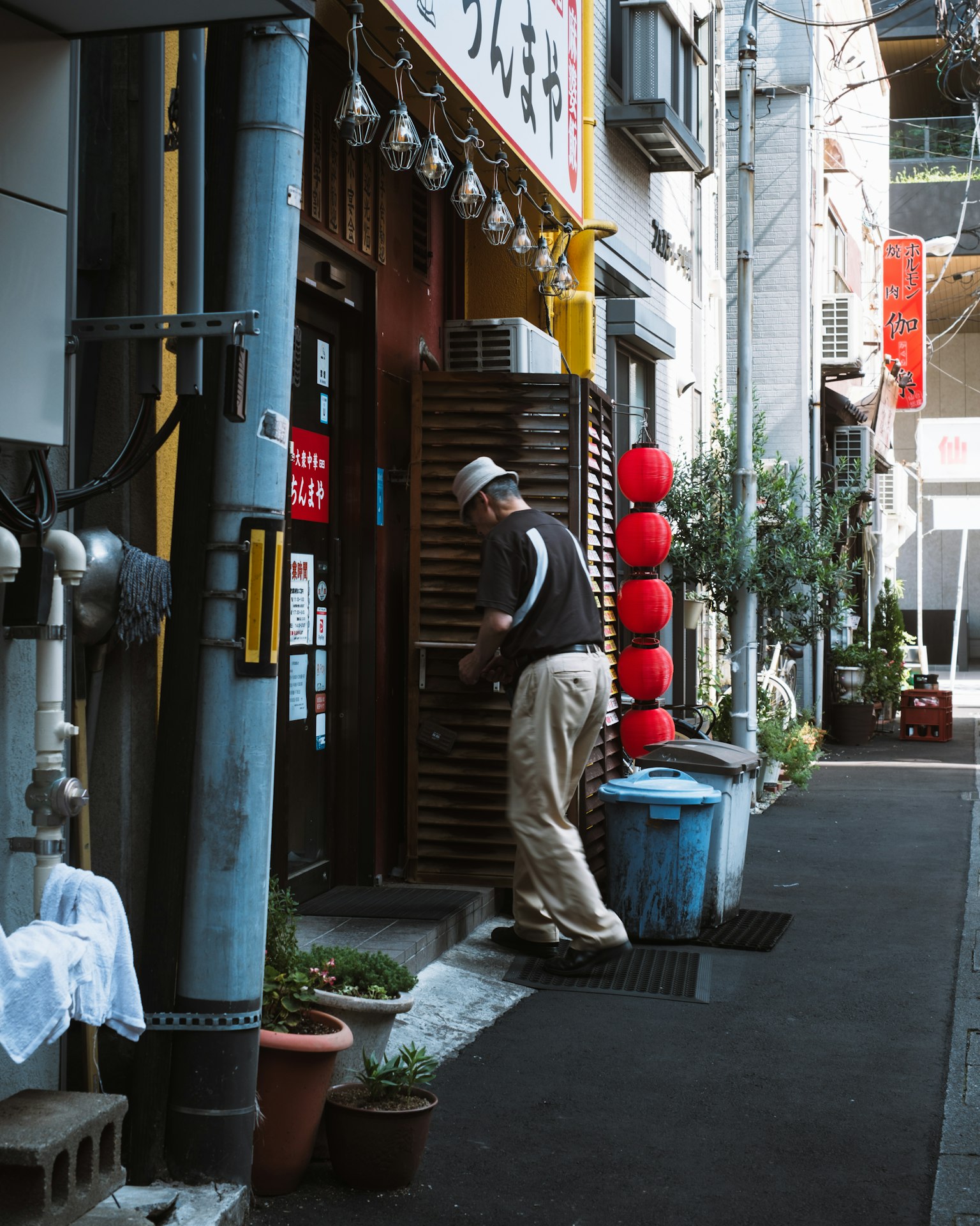 在狹窄巷道中日本餐廳入口處站著的男人和紅色燈籠