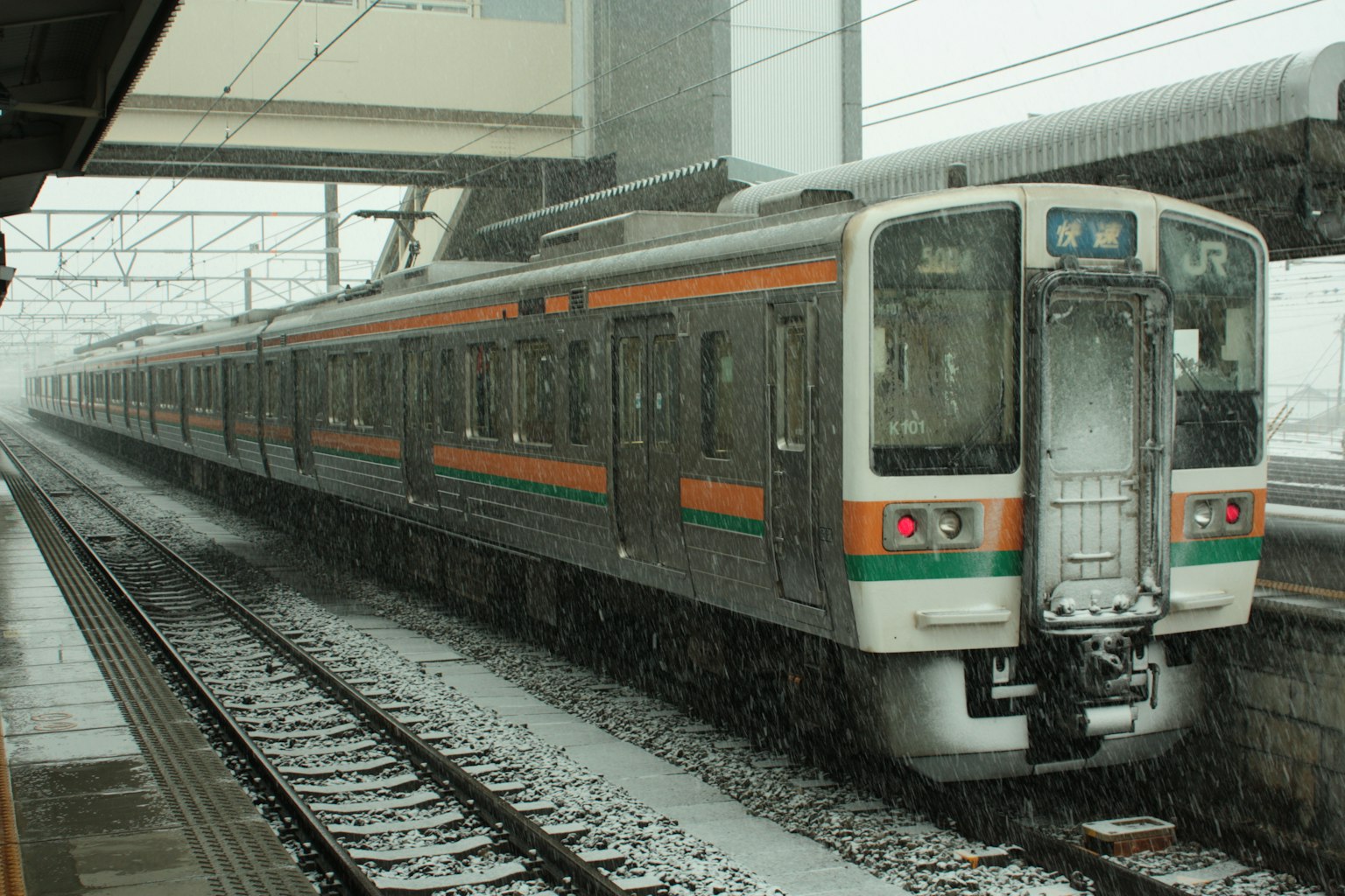 Train with orange and green stripes stopped in the snow