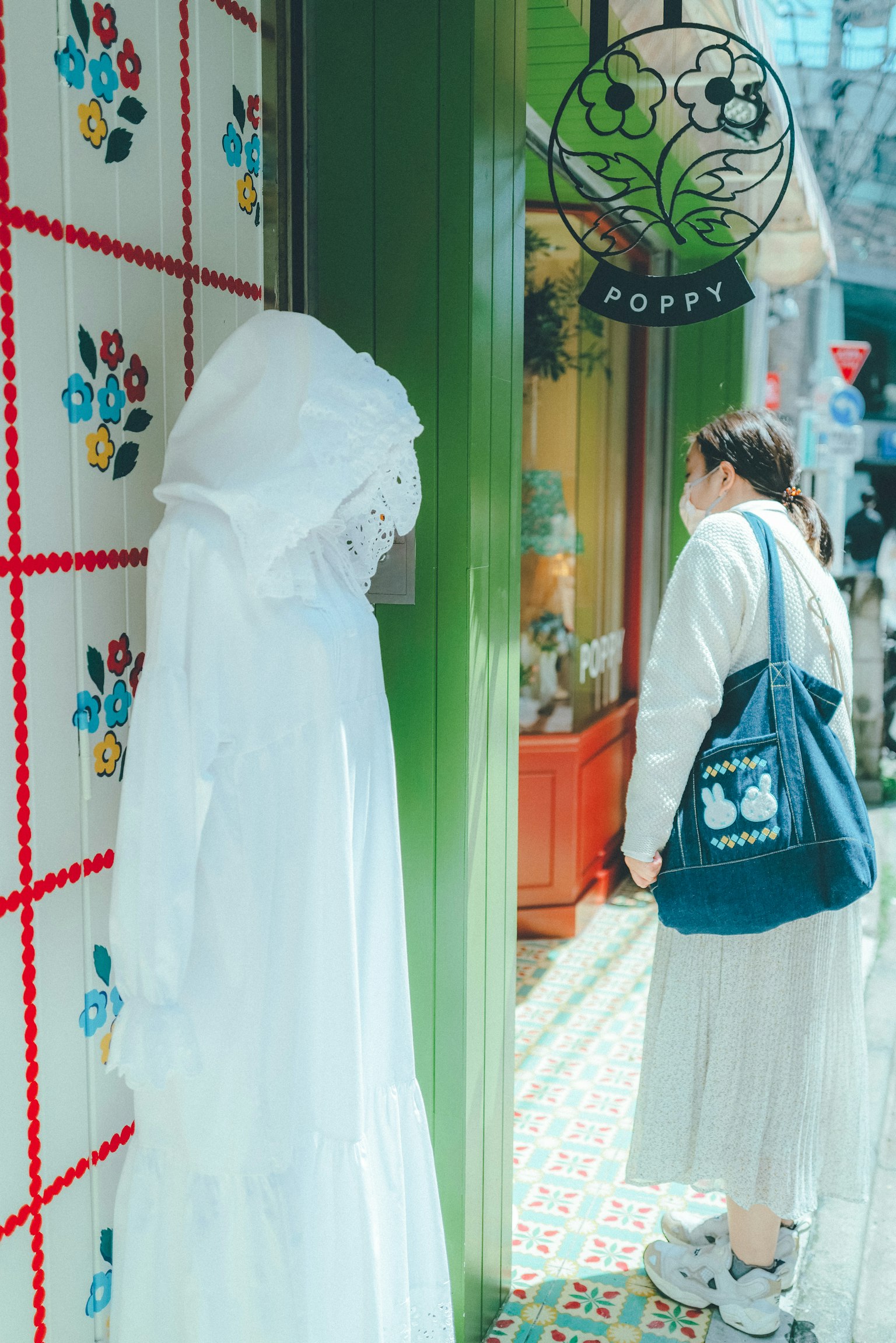 Una persona con ropa blanca está de pie frente a una tienda con una pared verde