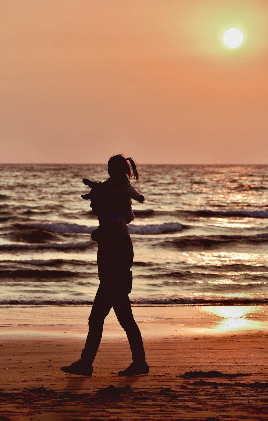 夕日に照らされた海辺を歩く親子のシルエット