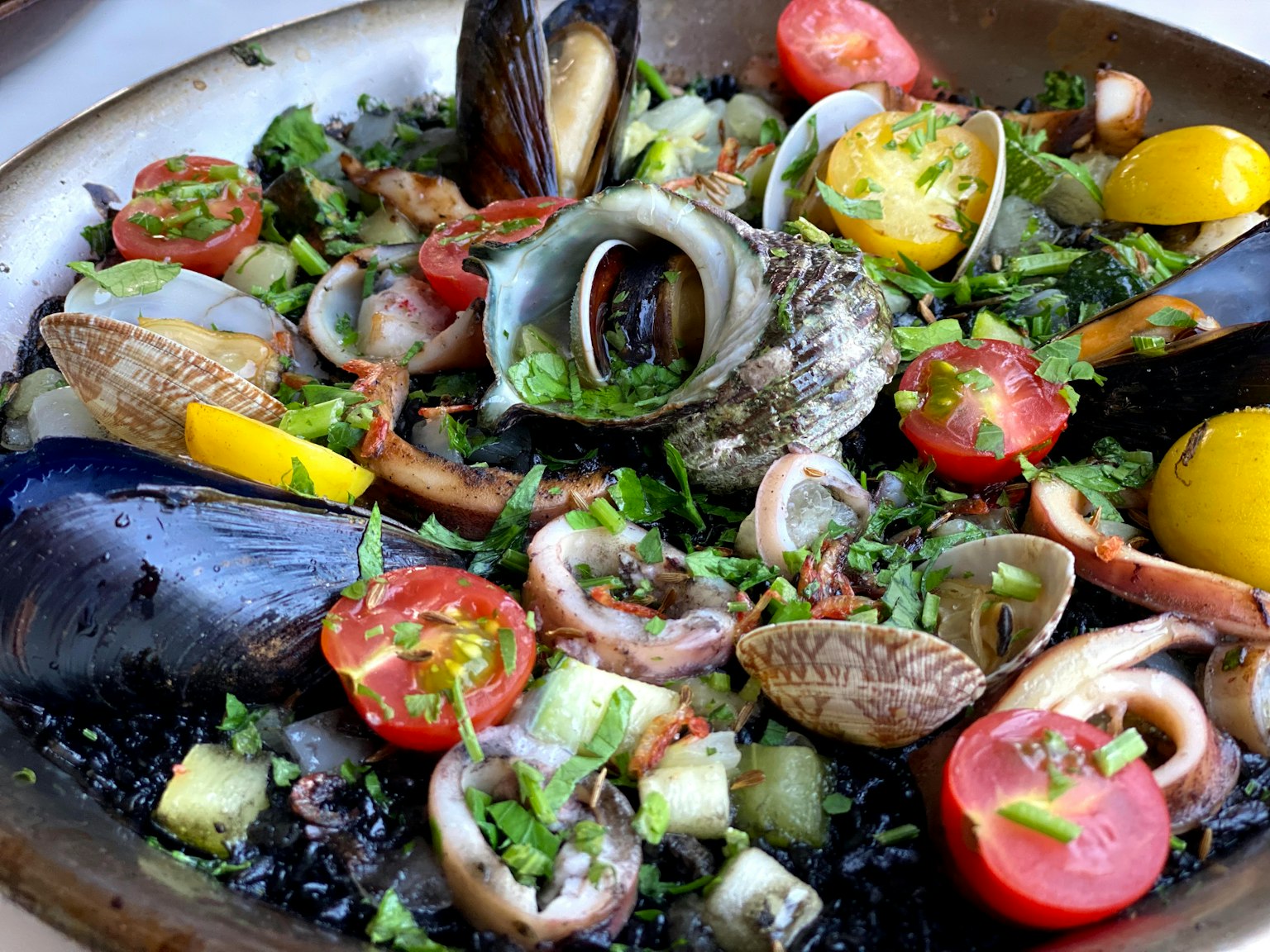 Un piatto di risotto nero con vari frutti di mare e pomodori