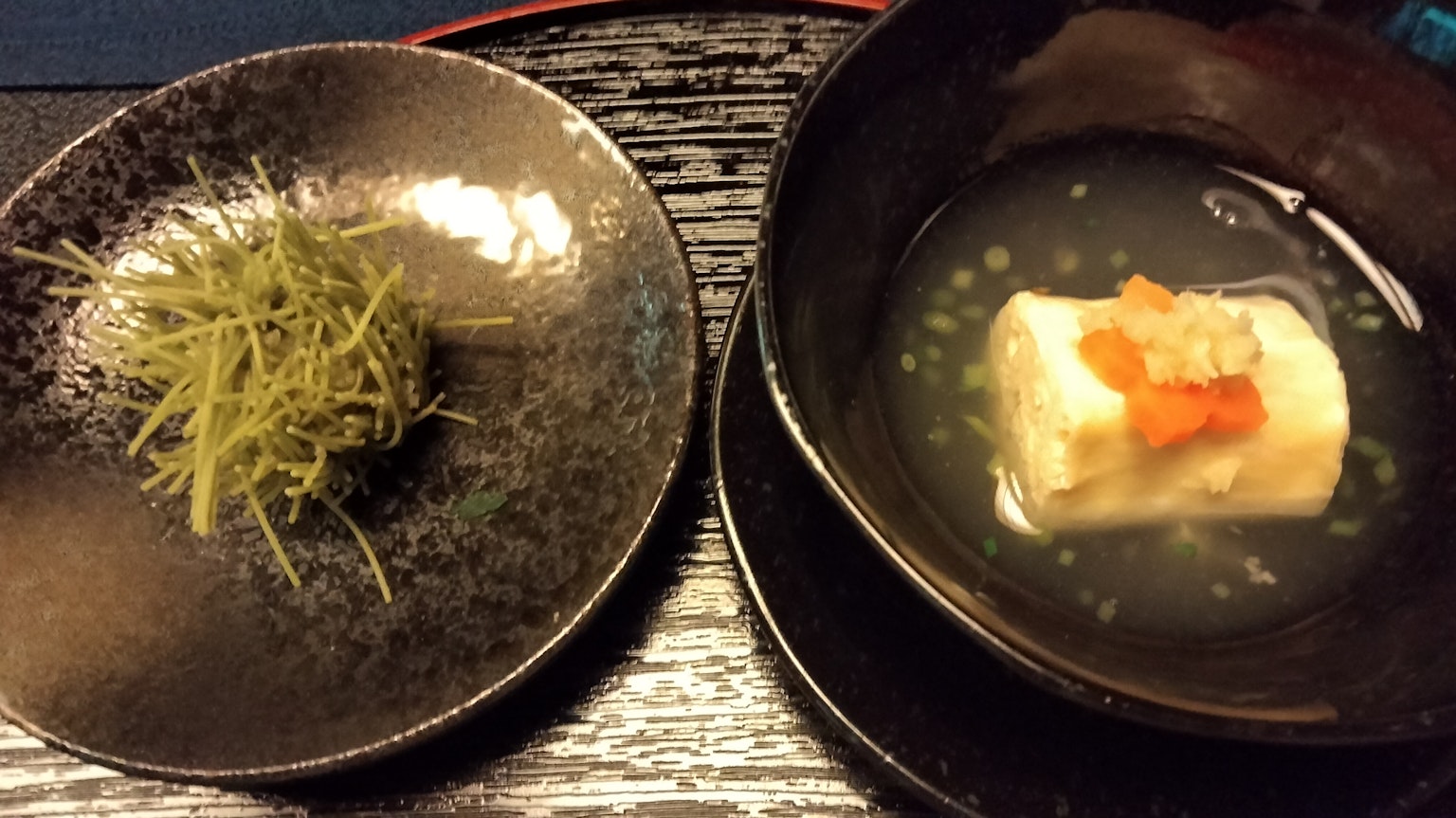 Une assiette noire avec du gingembre frais et un bol de plat de tofu