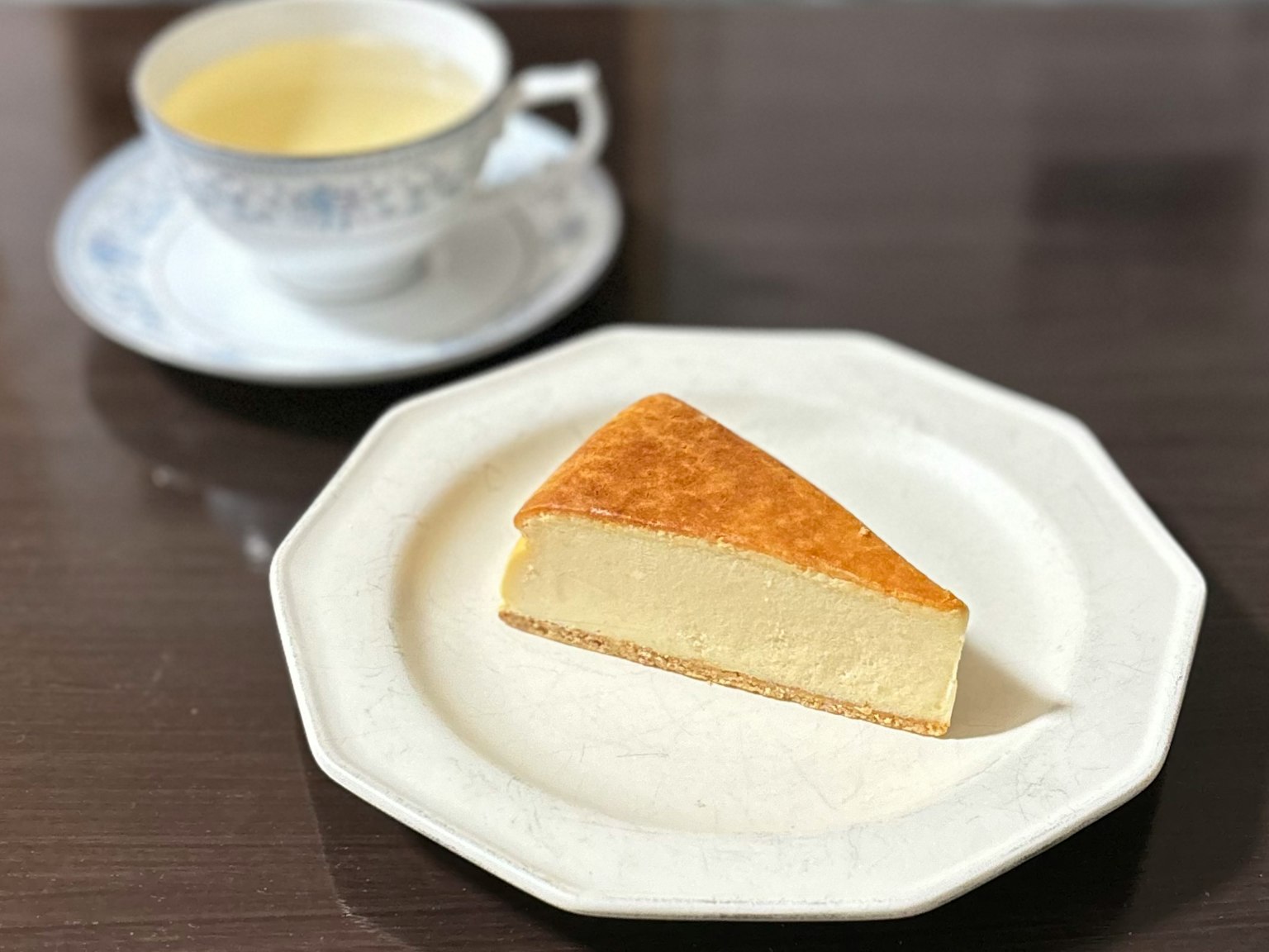 白色盤子上的起司蛋糕切片，背景有一杯茶