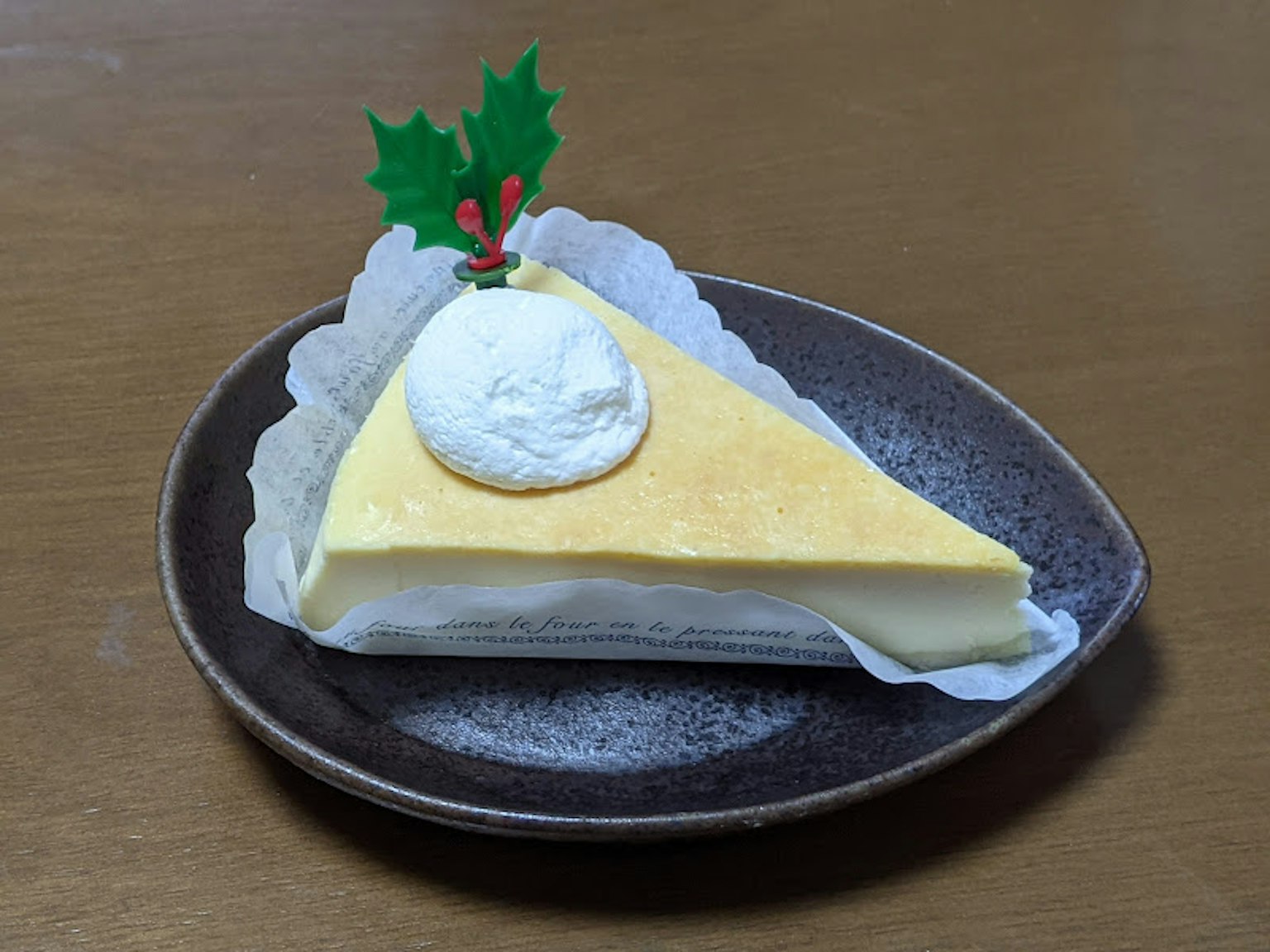 Fetta di cheesecake decorata con panna montata e foglie di agrifoglio