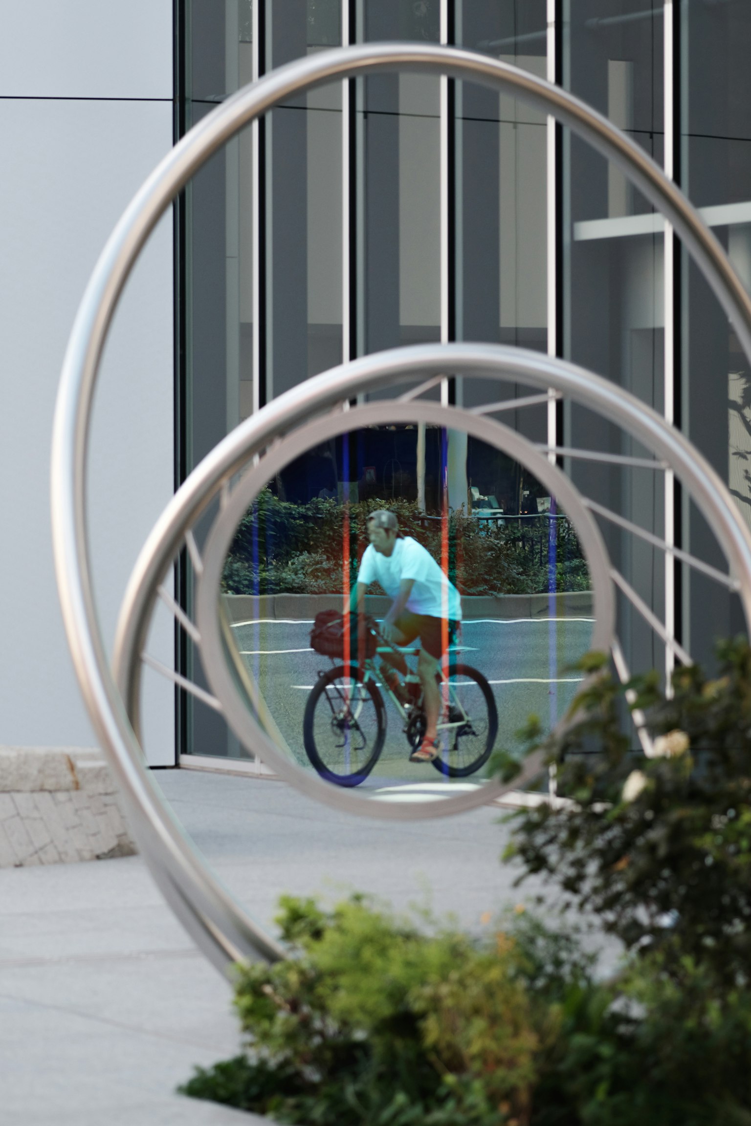 A man riding a bicycle seen through a circular metal sculpture