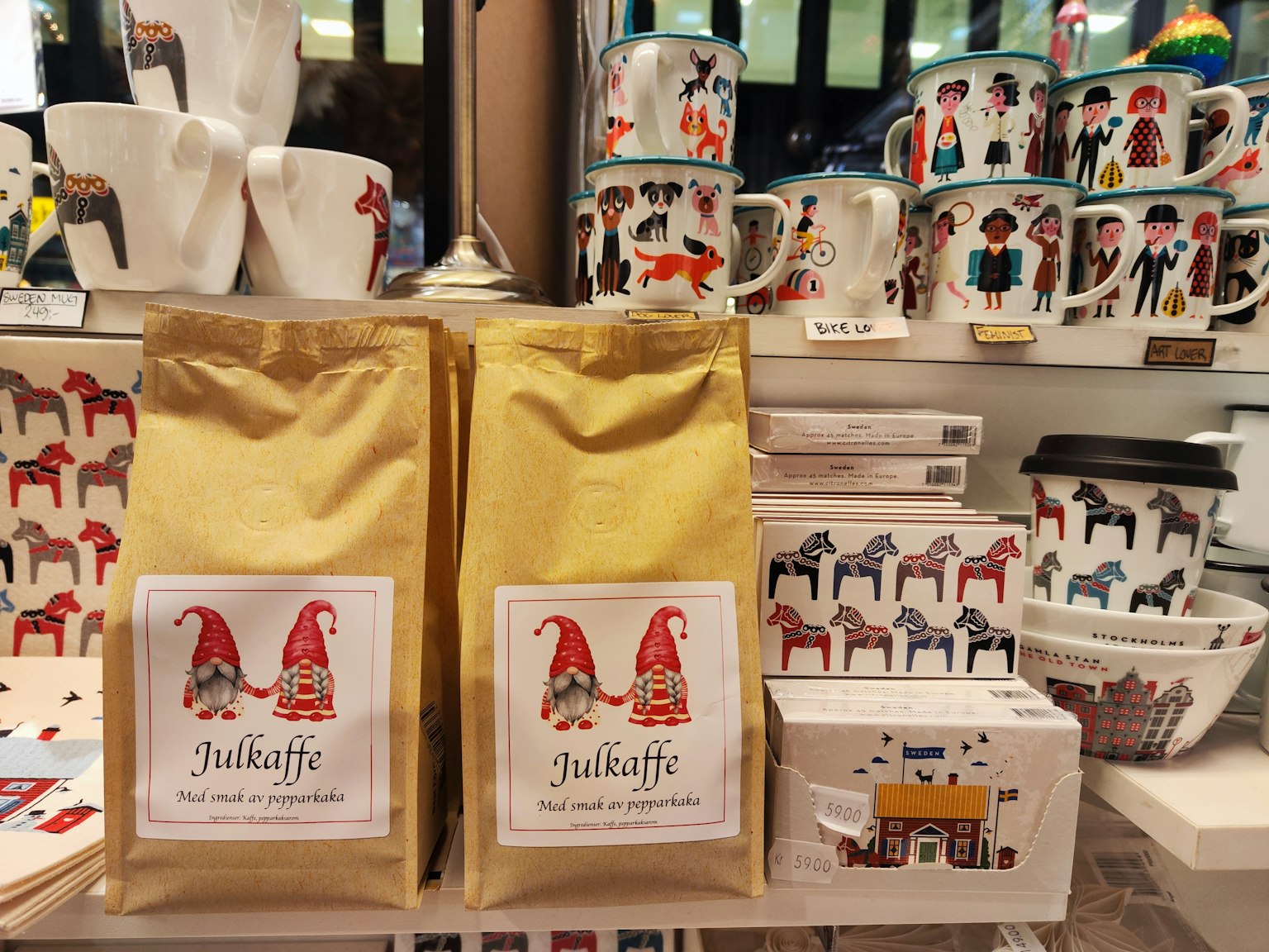 Dos bolsas de café con ilustraciones de gnomos y tazas coloridas exhibidas en una tienda