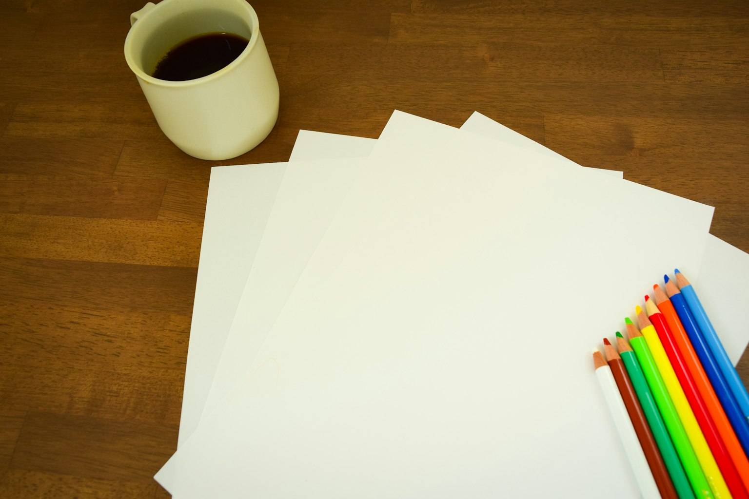 Meja dengan kertas kosong dan pensil warna-warni di samping secangkir kopi