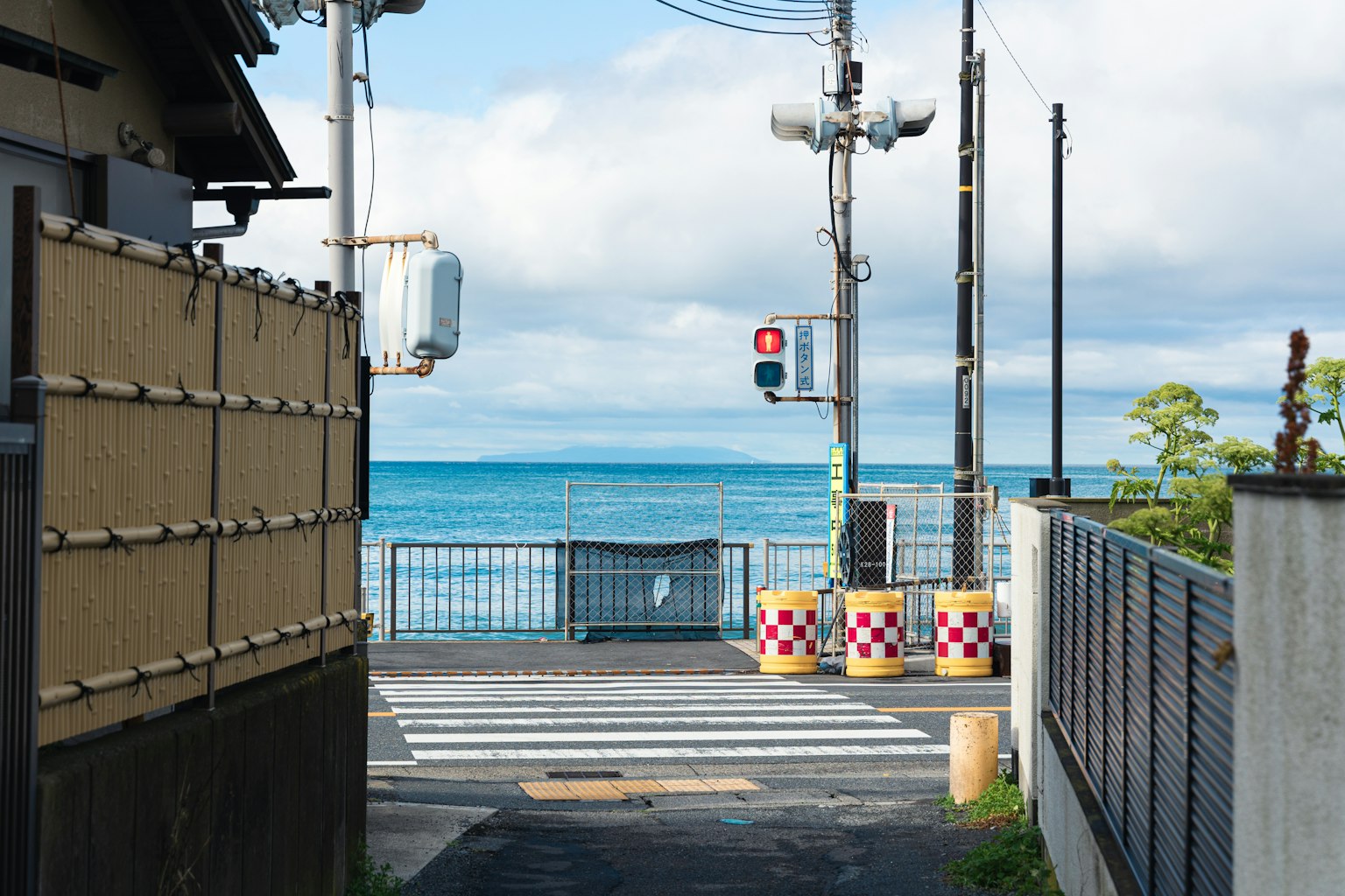 Vue pittoresque de la mer et du ciel bleus avec un passage piéton et un feu de circulation au premier plan entouré de maisons et de poteaux électriques