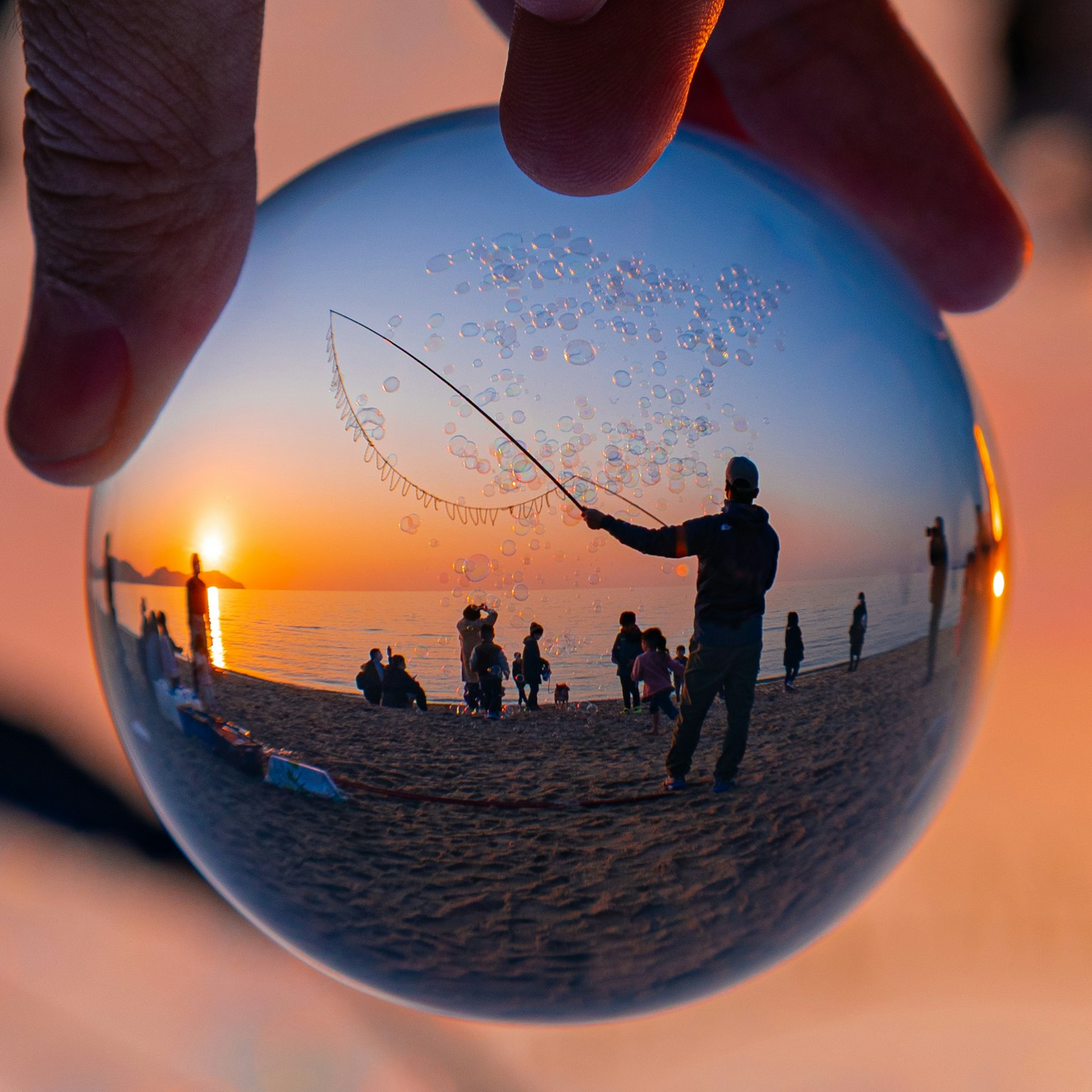 A crystal ball reflecting a person fishing at sunset by the beach