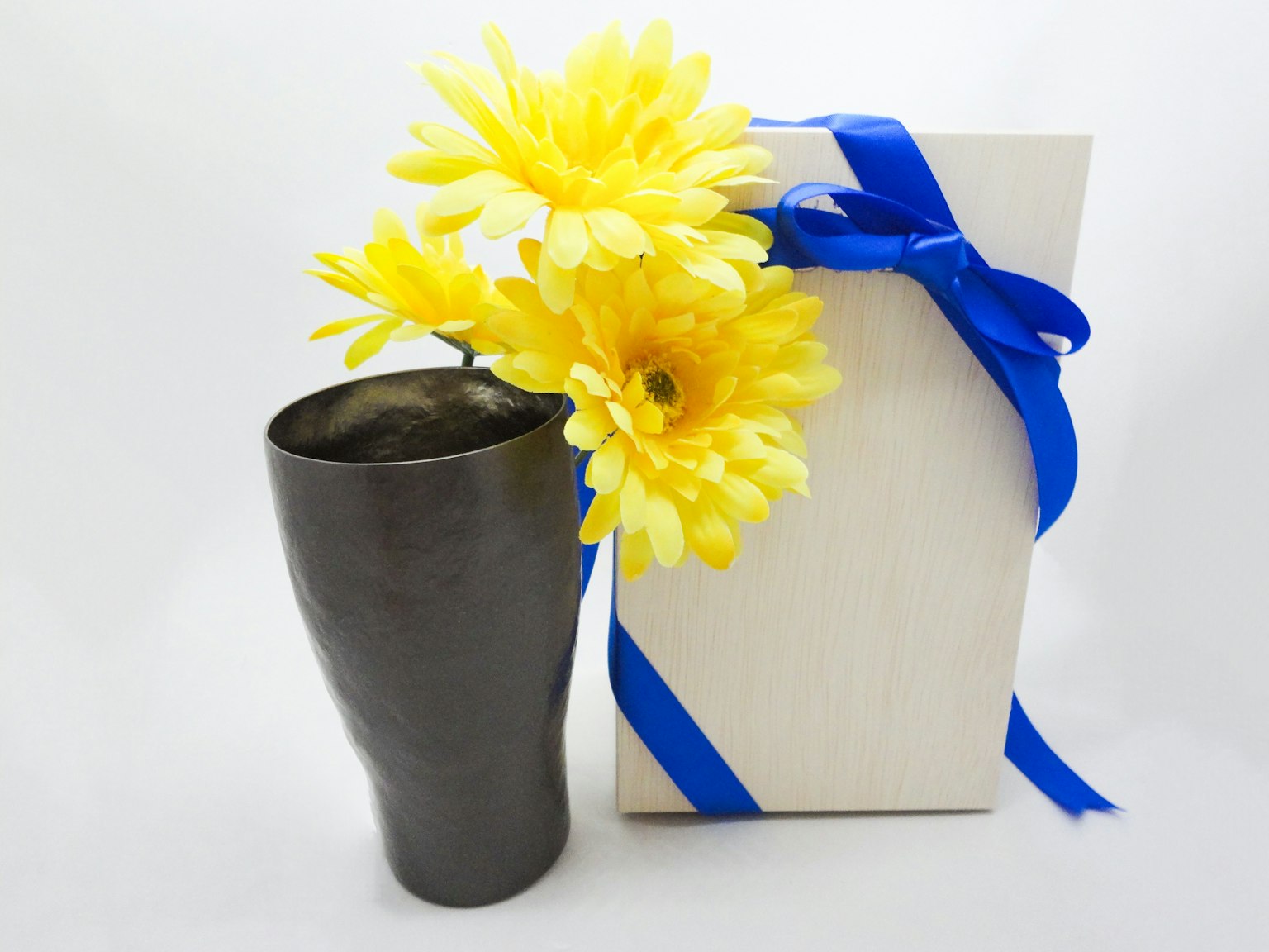 Vaso nero con fiori gialli accanto a una scatola regalo legata con un nastro blu