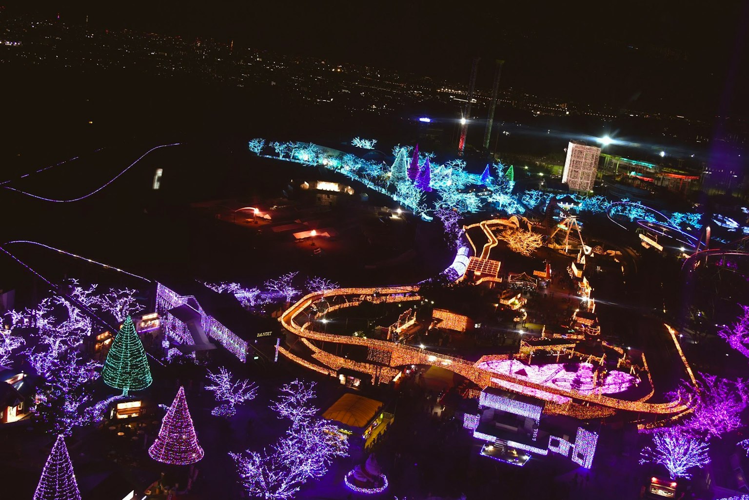Vista aerea di un parco divertimenti illuminato di notte con luci colorate e alberi decorati
