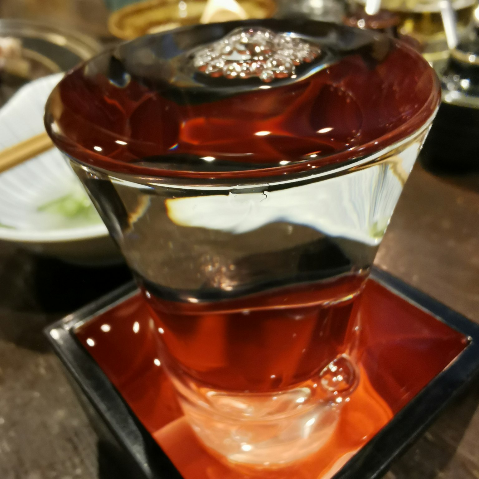 Bellissimo bicchiere di sakè rosso pieno di liquido trasparente su una base nera
