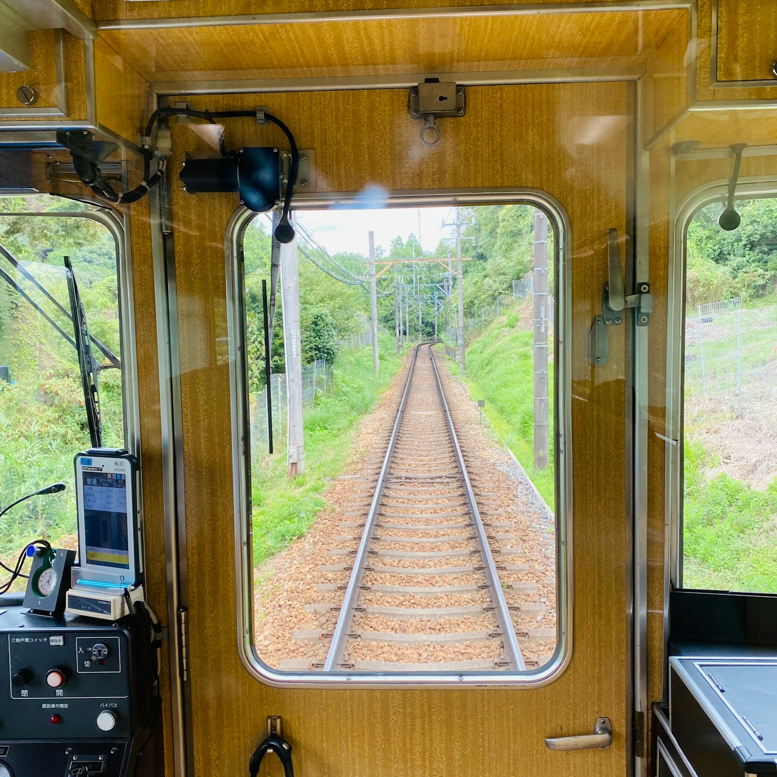 View of railway tracks from inside a train cabin with lush greenery