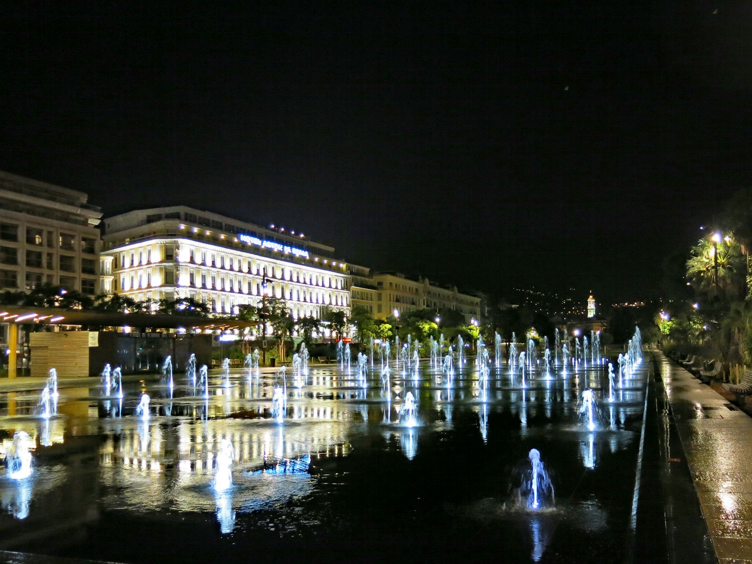Stadtansicht bei Nacht mit beleuchteten Brunnen und Spiegelungen