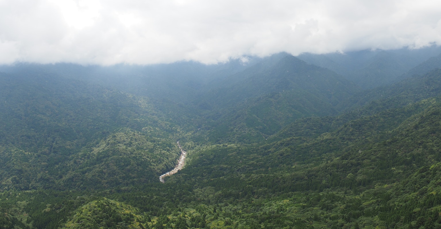 Pegunungan hijau subur dengan sungai berkelok di bawah langit mendung
