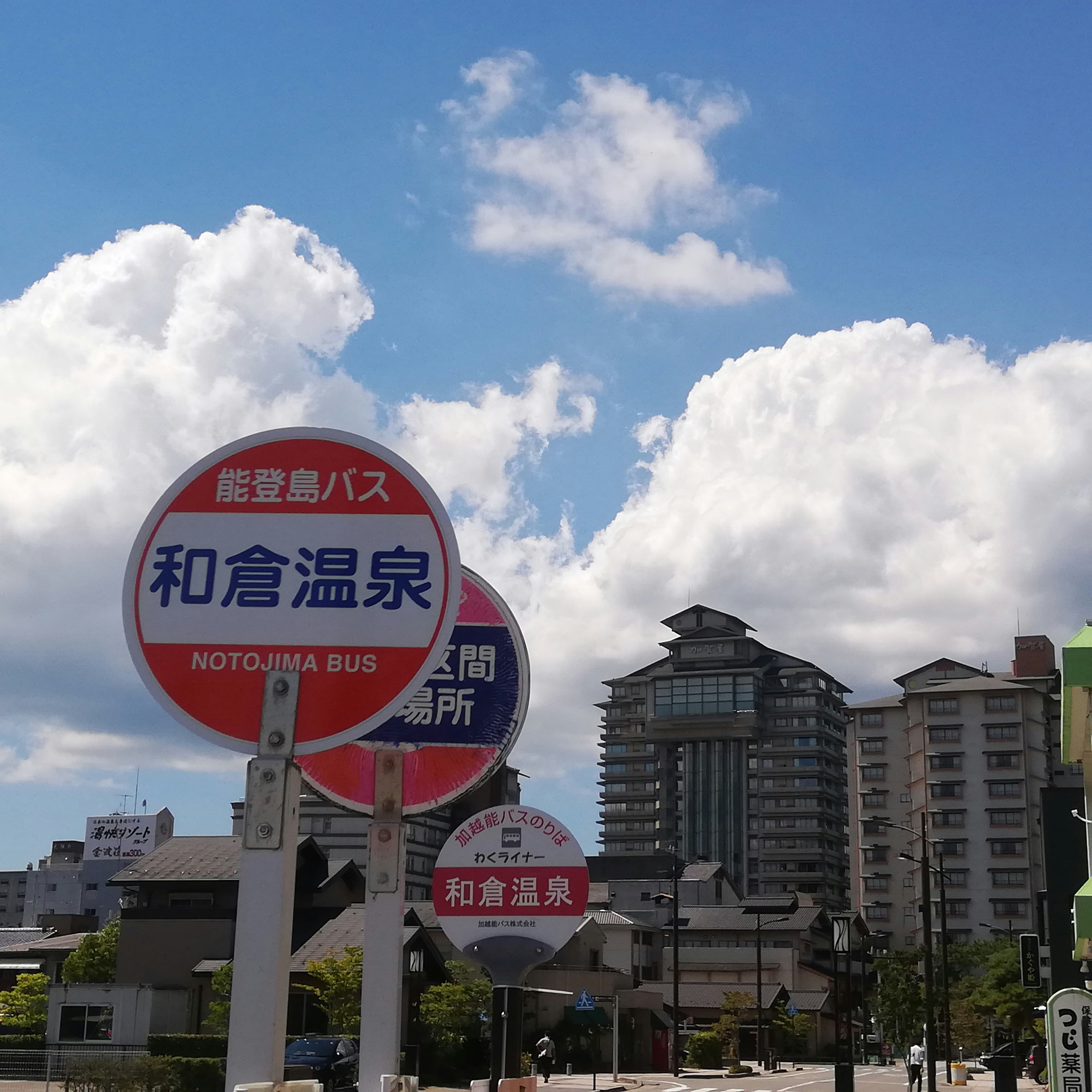 雲の下に立つ和倉温泉のバス停標識と温泉街の建物