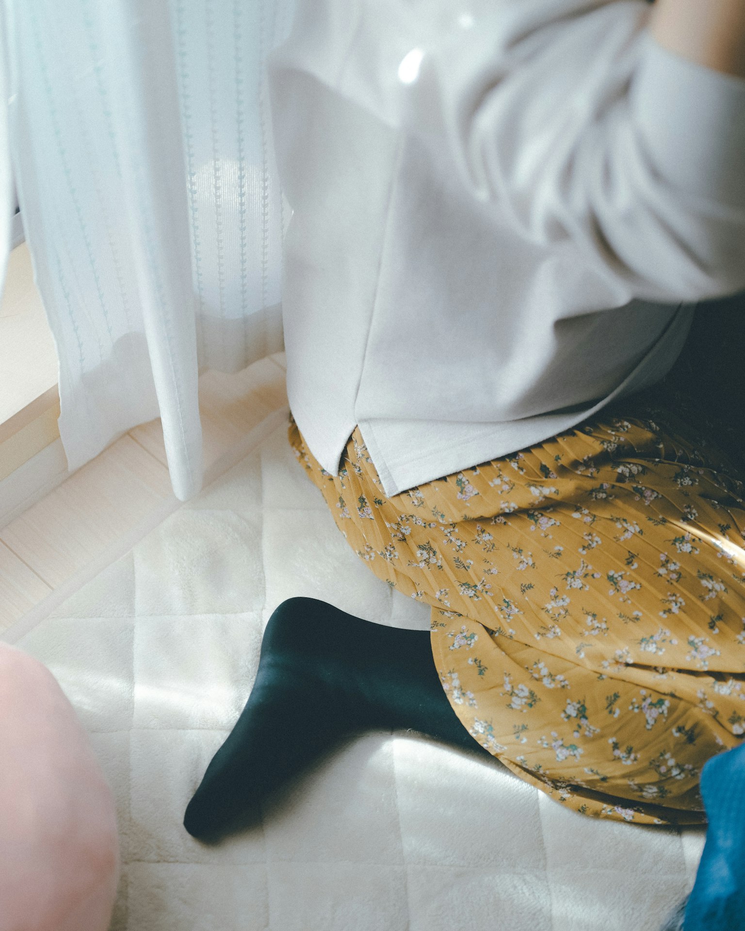 Partial view of a person sitting by a window wearing a patterned skirt and black socks