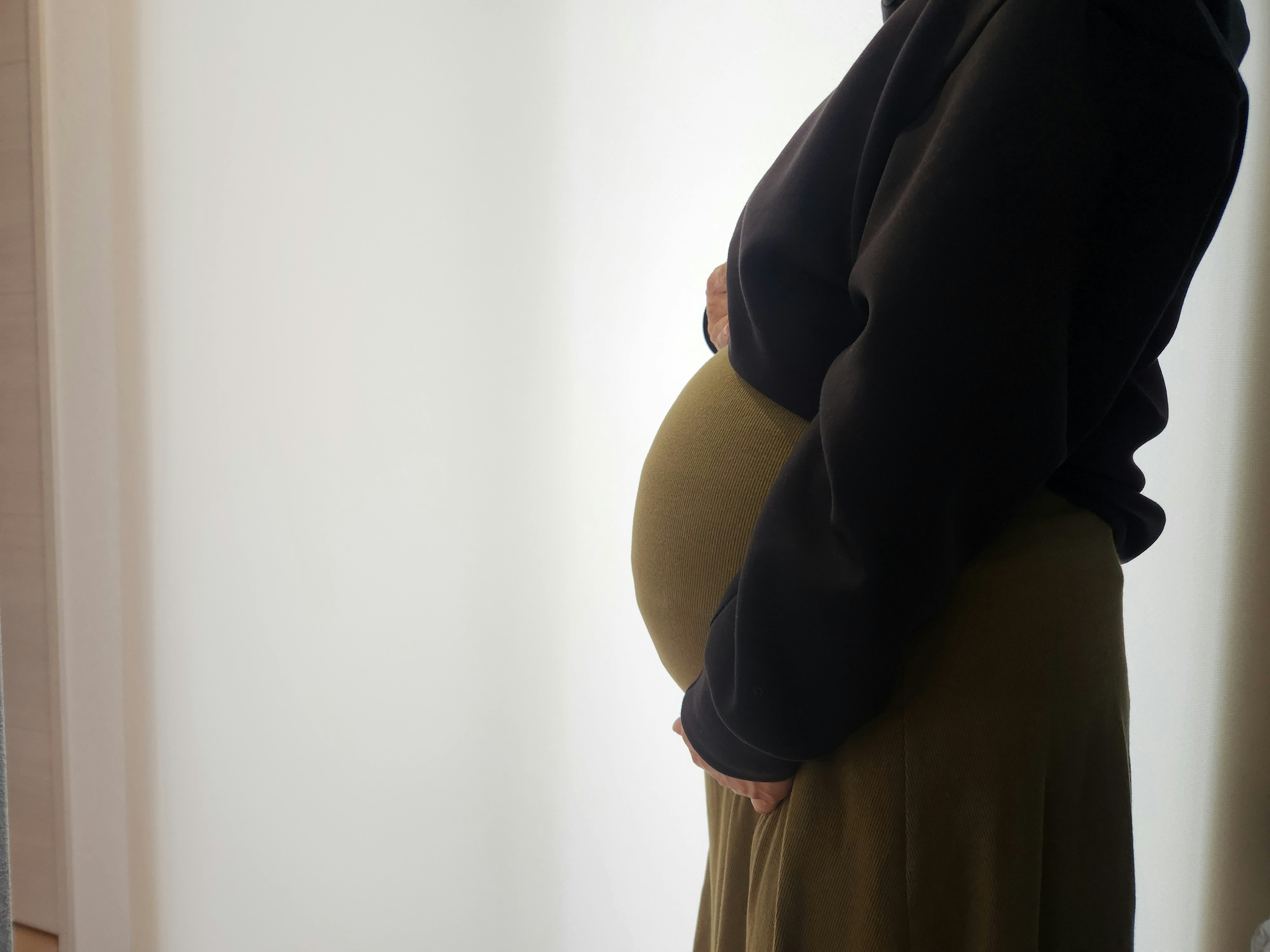 妊婦の女性が窓辺で手をお腹に添える