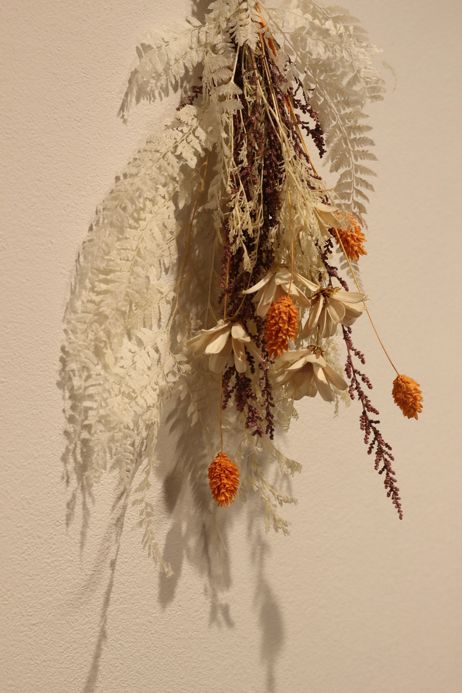 干花装饰，白色叶子和橙色花朵悬挂在墙上