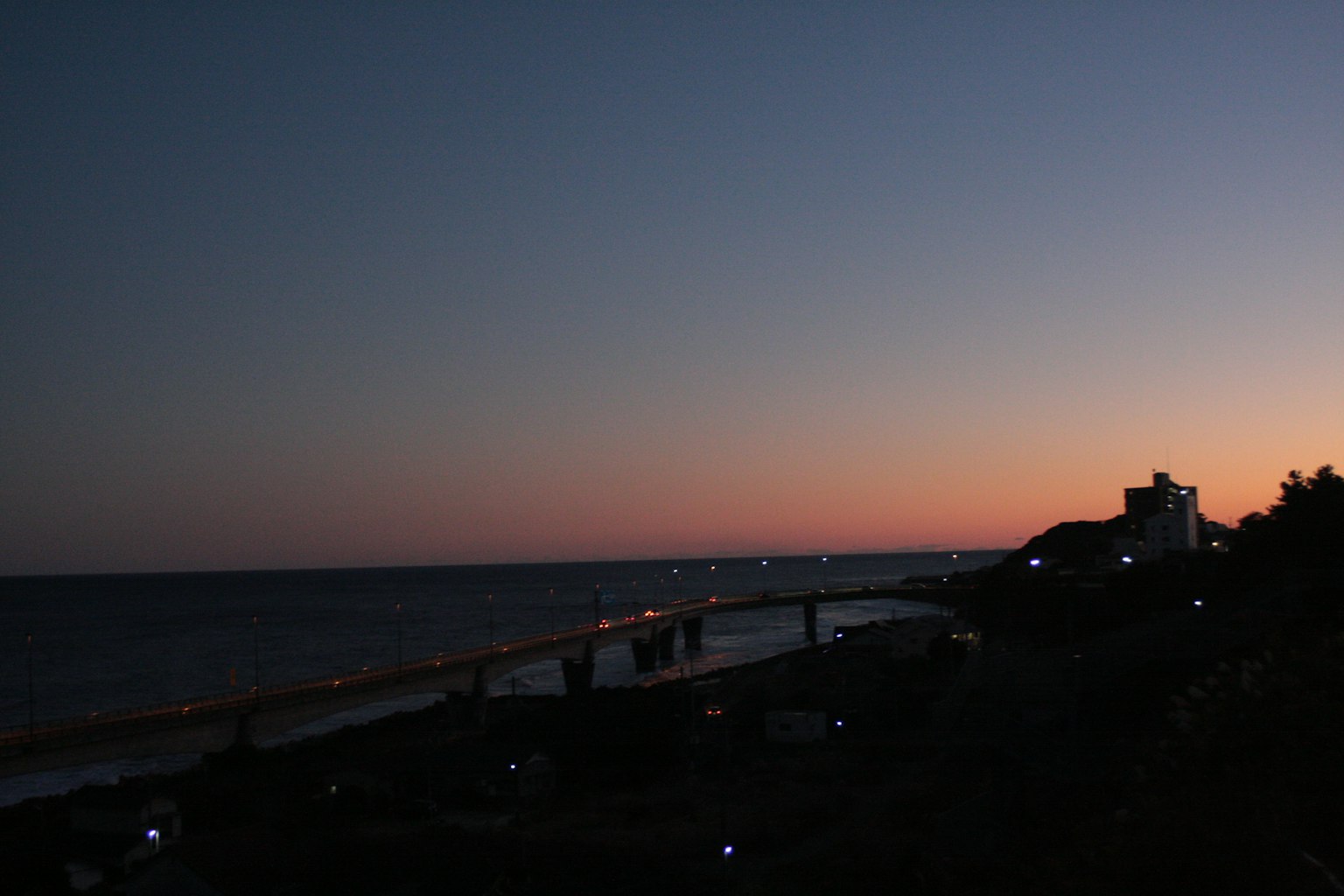 Coastal view at twilight with a serene ocean and distant lights