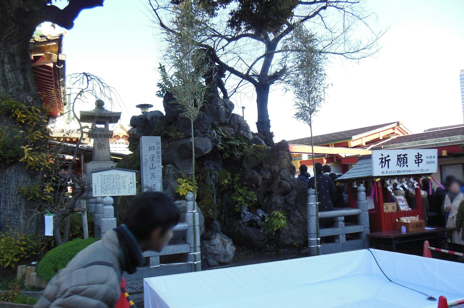 Vista panoramica di un cortile di santuario con grandi rocce e alberi molte persone in movimento
