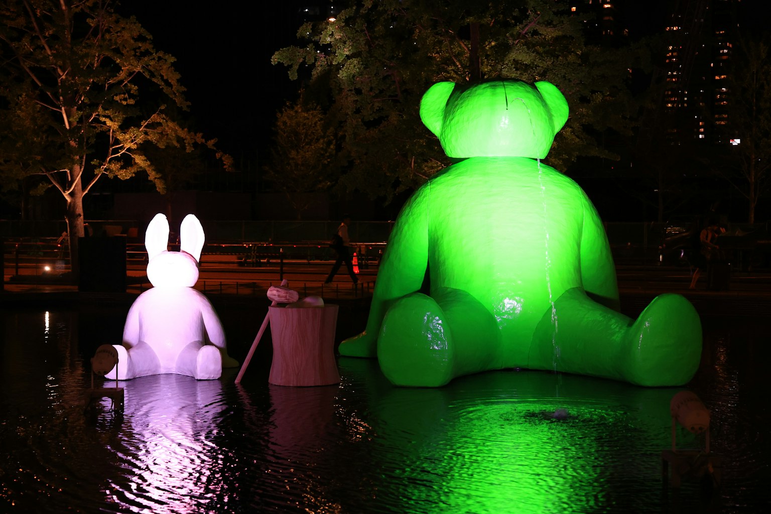 Grande scultura di orso verde e coniglio bianco che brillano in uno stagno notturno