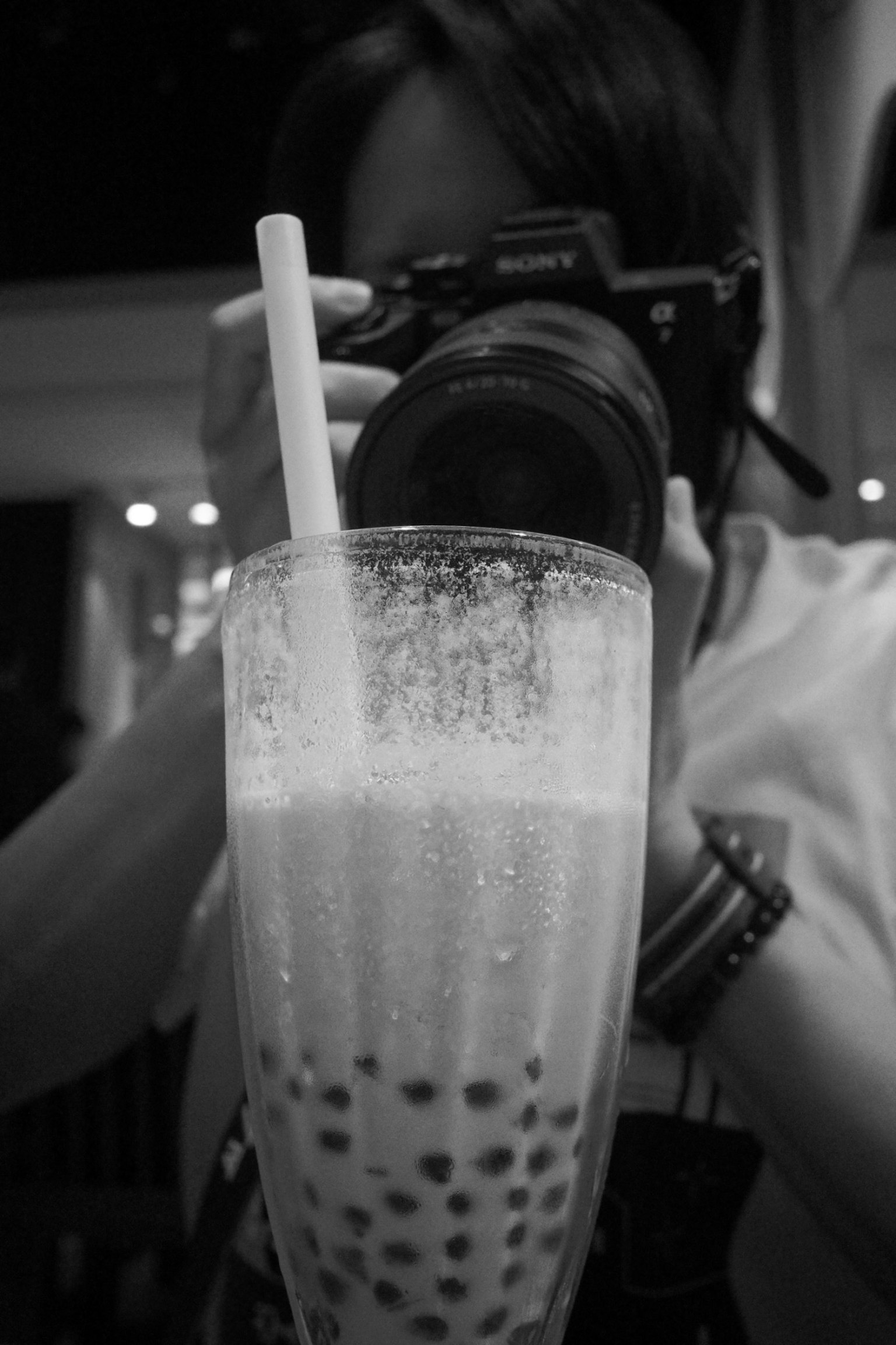 カメラを持つ人物とタピオカドリンクのモノクロ写真