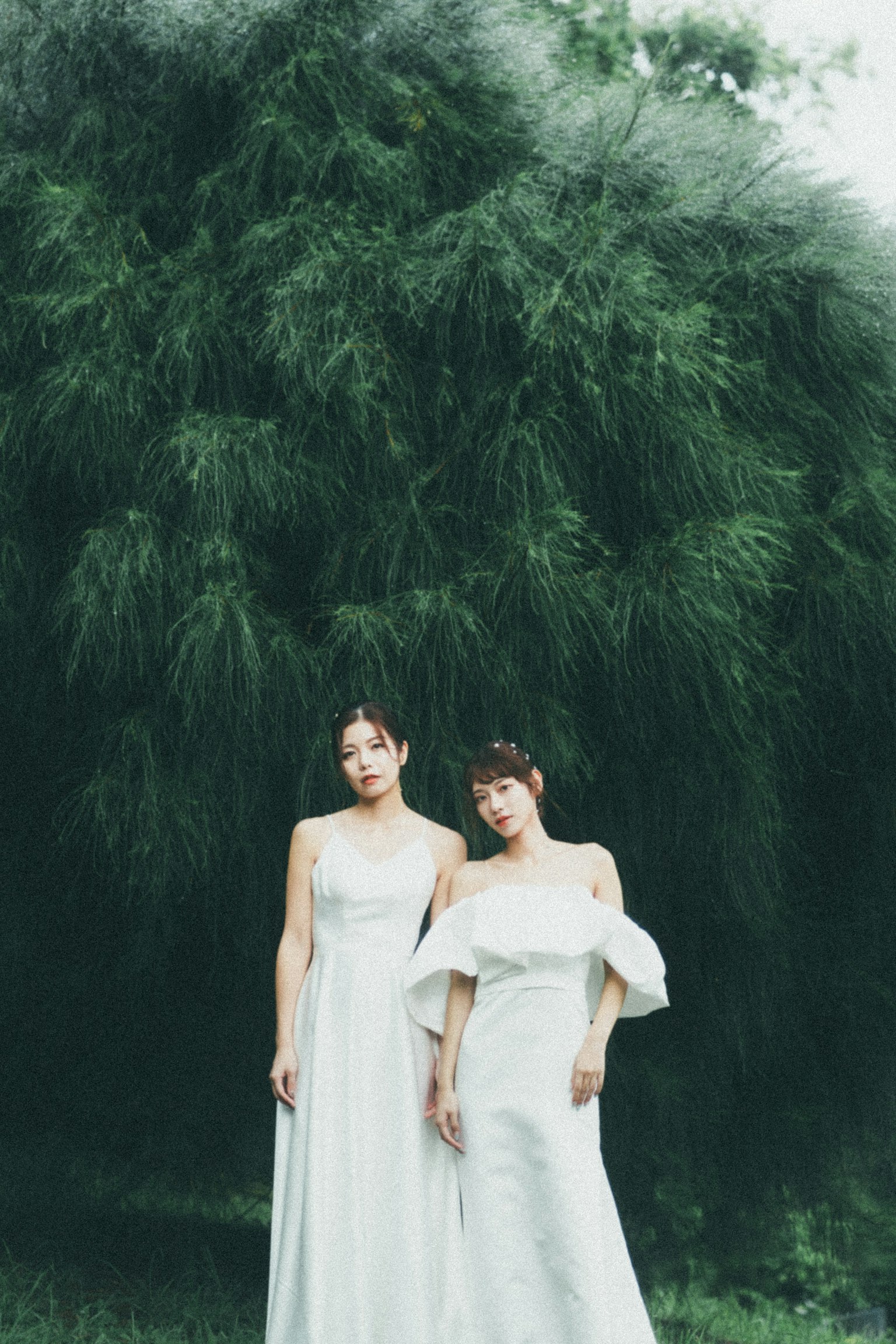 兩位穿著白色裙子的女性站在綠色背景前