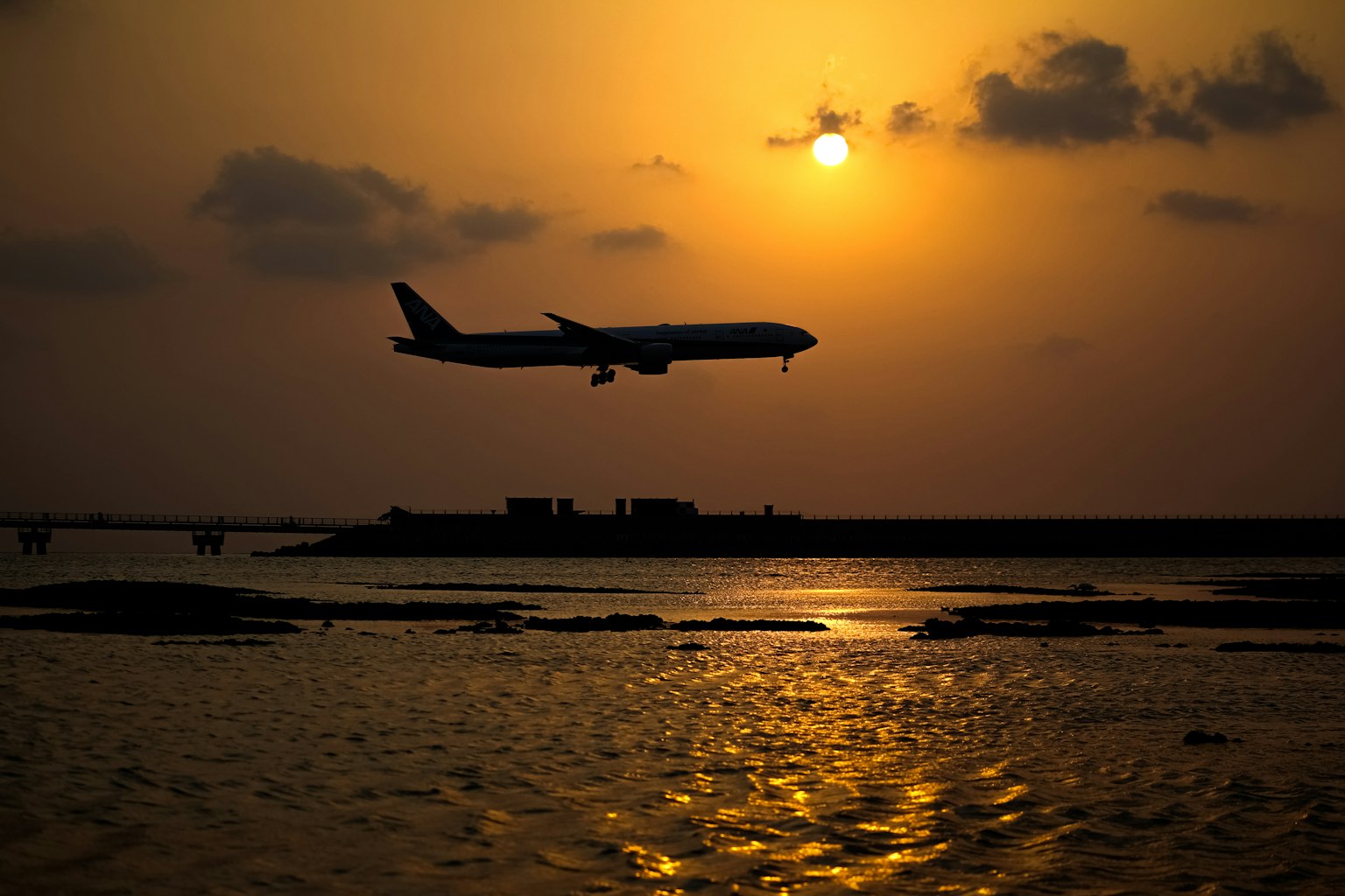 Avion atterrissant en silhouette contre un coucher de soleil se reflétant sur l'eau