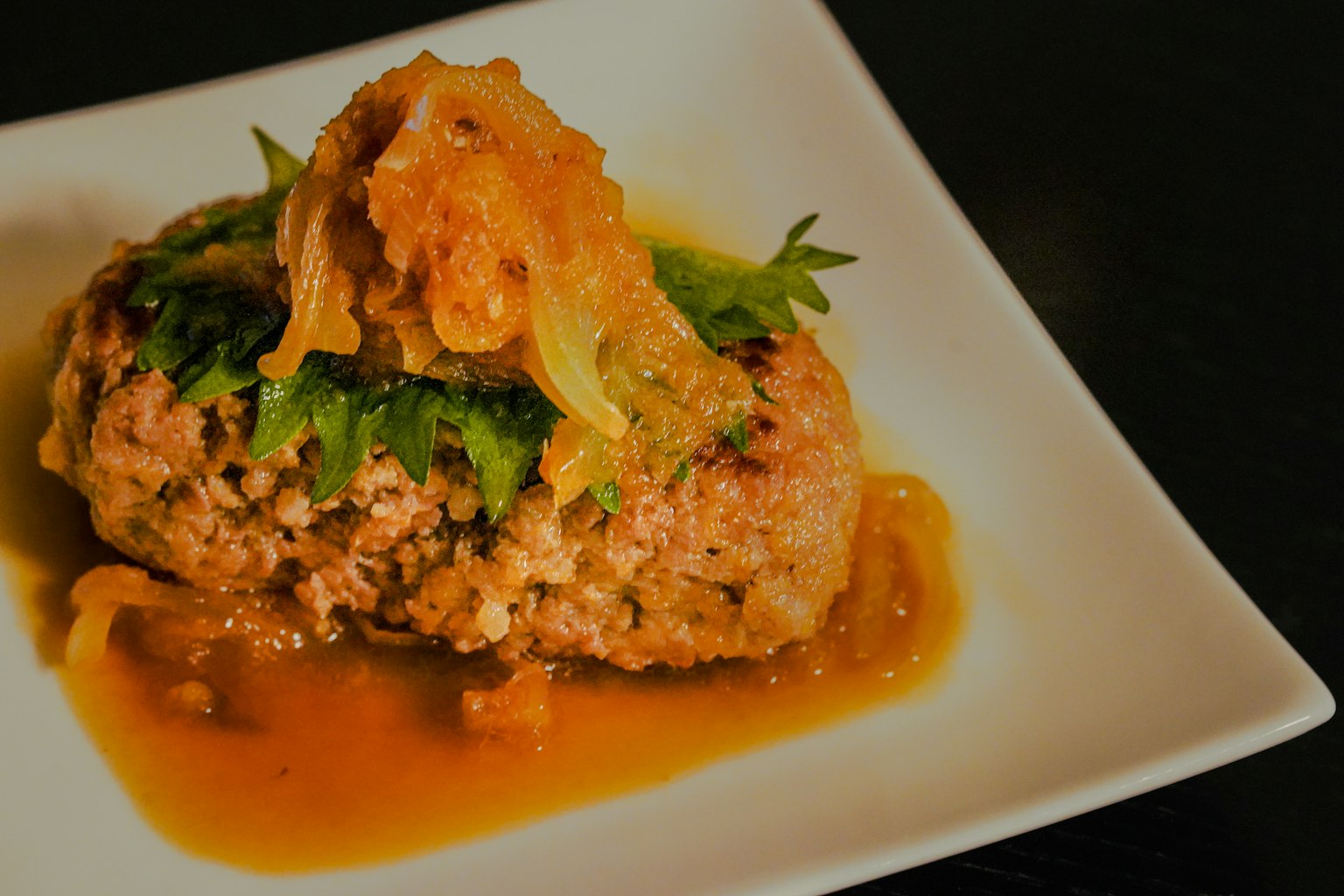 Delicious meatball topped with herbs and tangy sauce on a white plate
