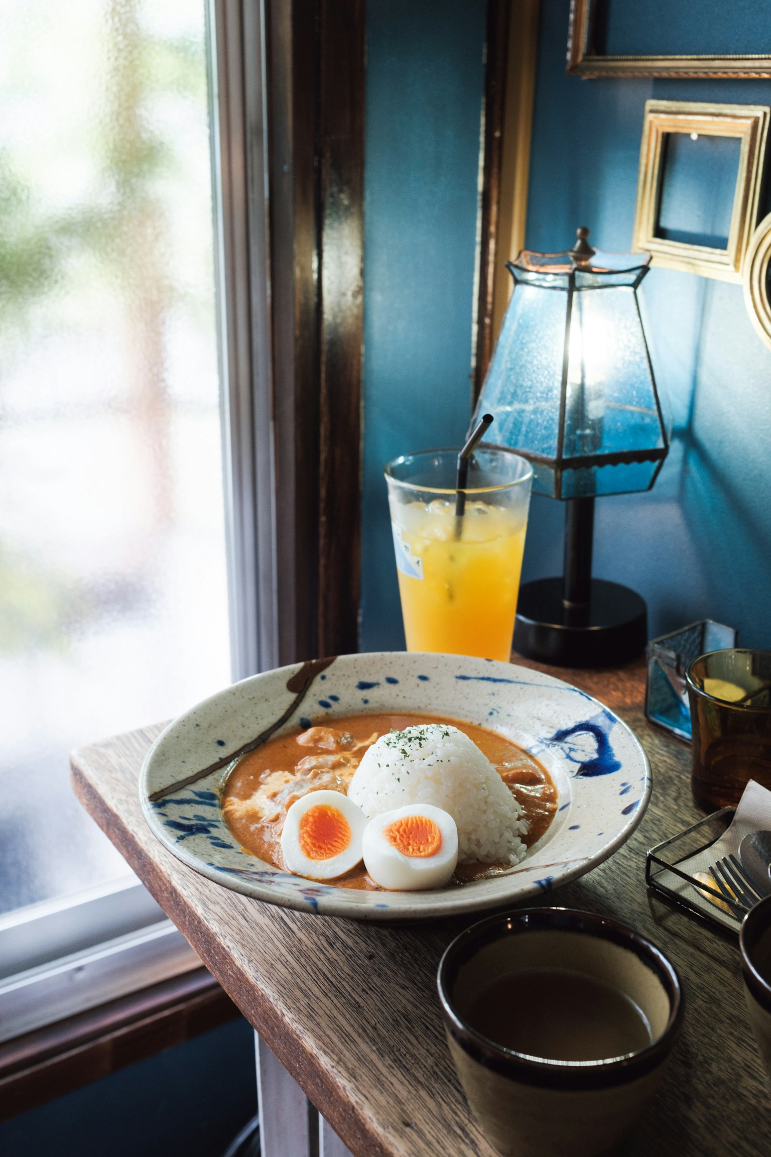 Piring makanan dengan telur setengah matang dan minuman di atas meja kayu di depan dinding biru