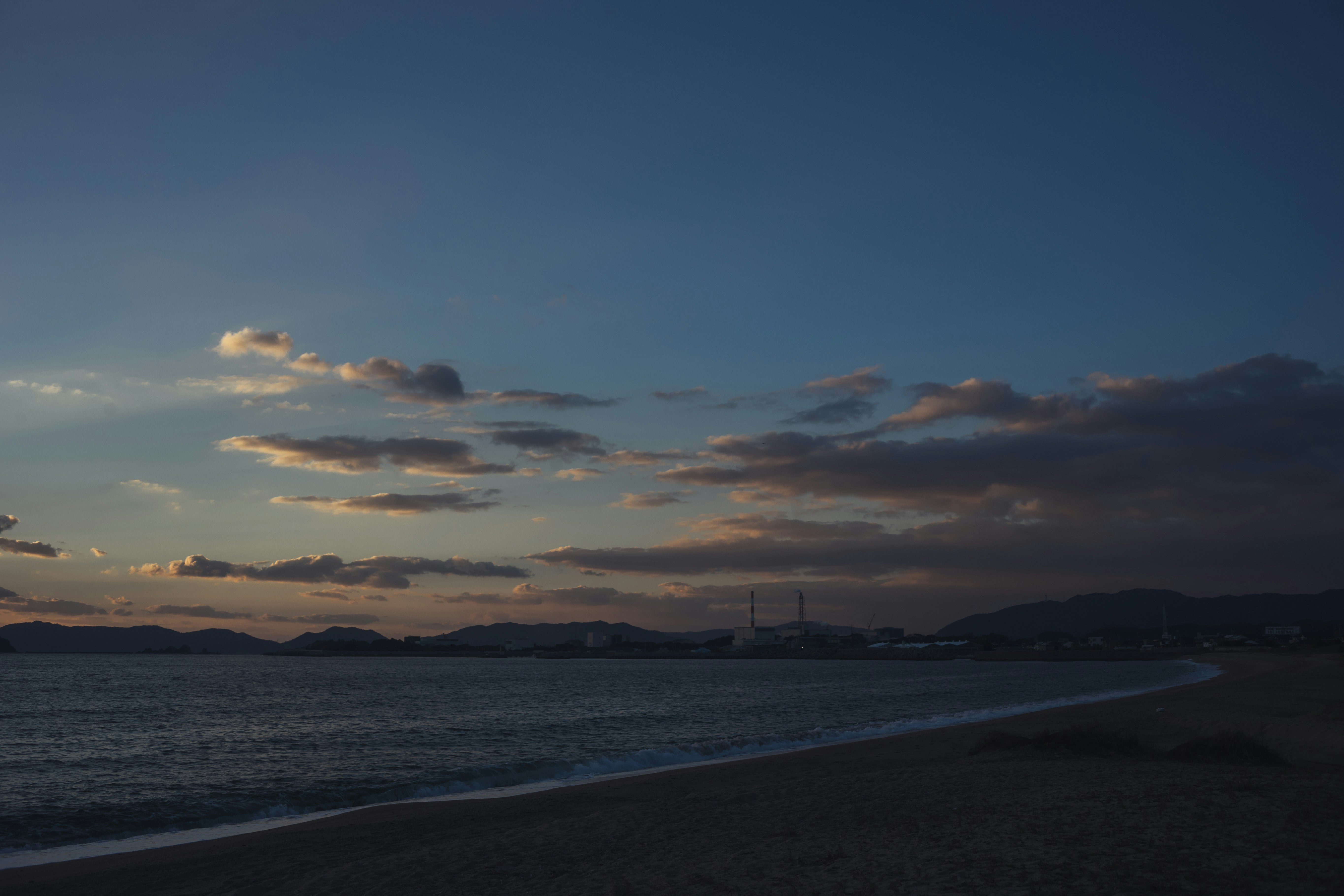 夕暮れの海辺と遠くの工業地帯のシルエット