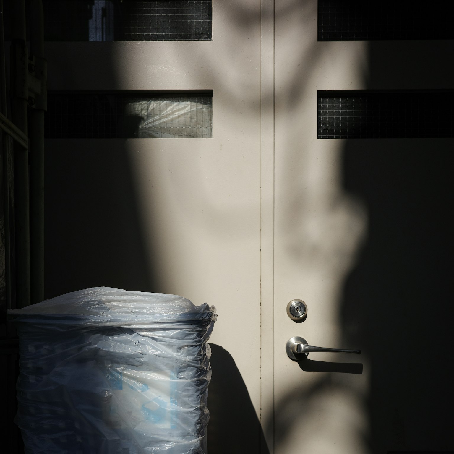 Scene with a door casting shadows and a trash bin